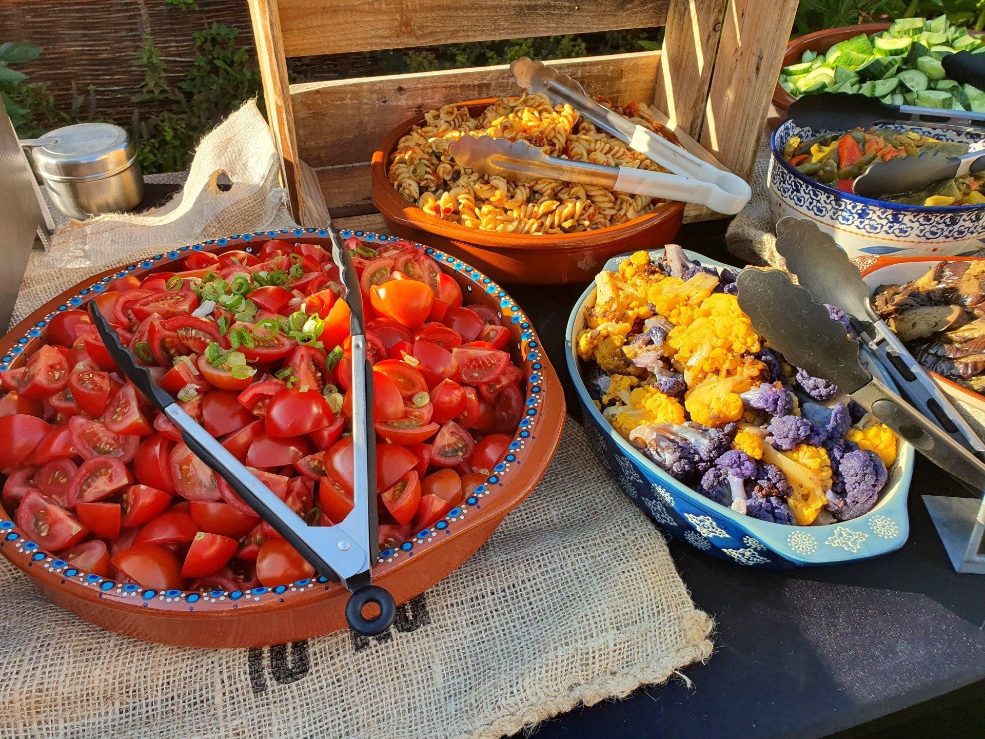 Buffet met salades van tomaten, pasta, gele en paarse bloemkool en andere gerechten.