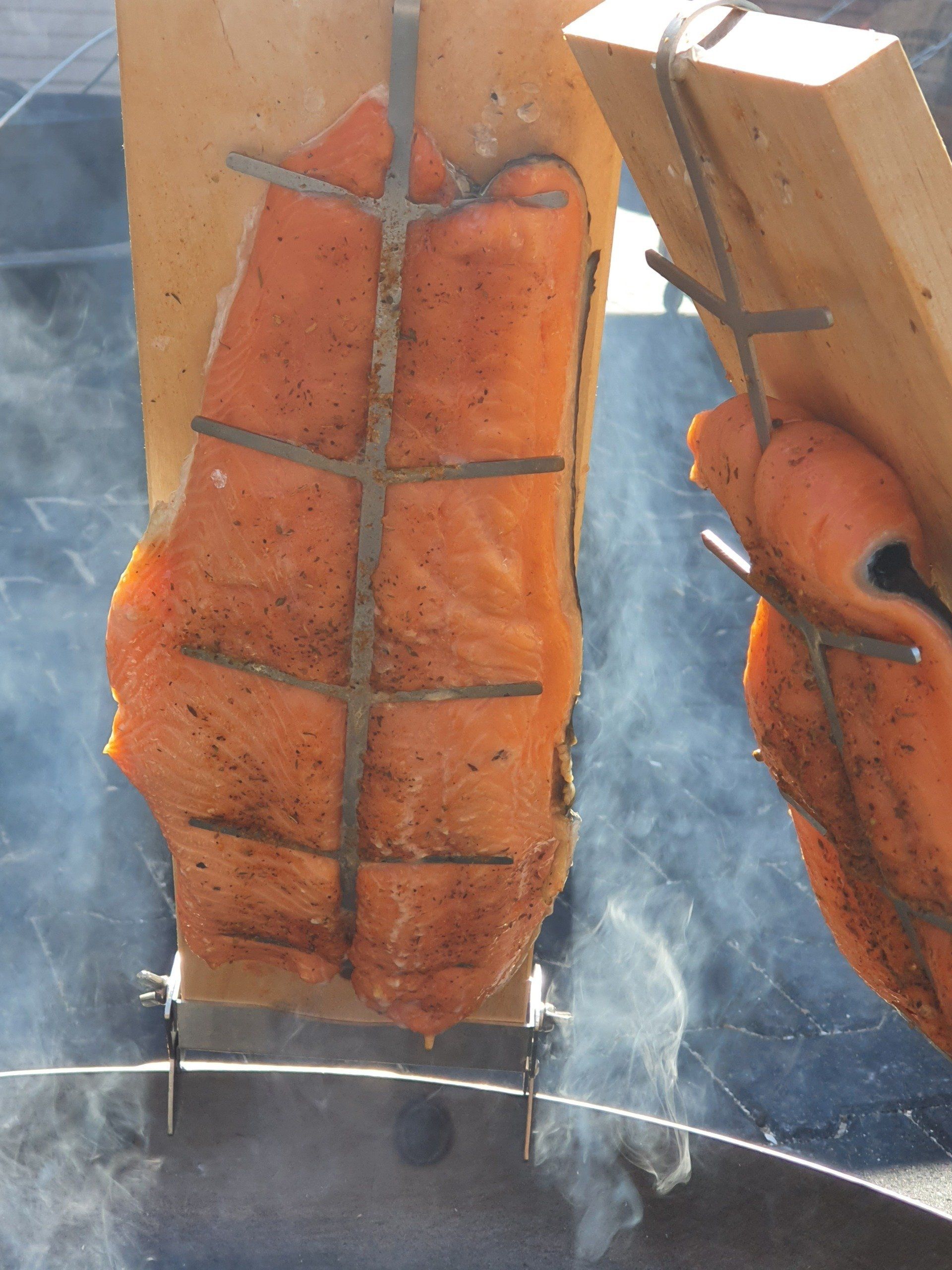 Zalmfilets worden gerookt op houten planken, vastgehouden door metalen frames.