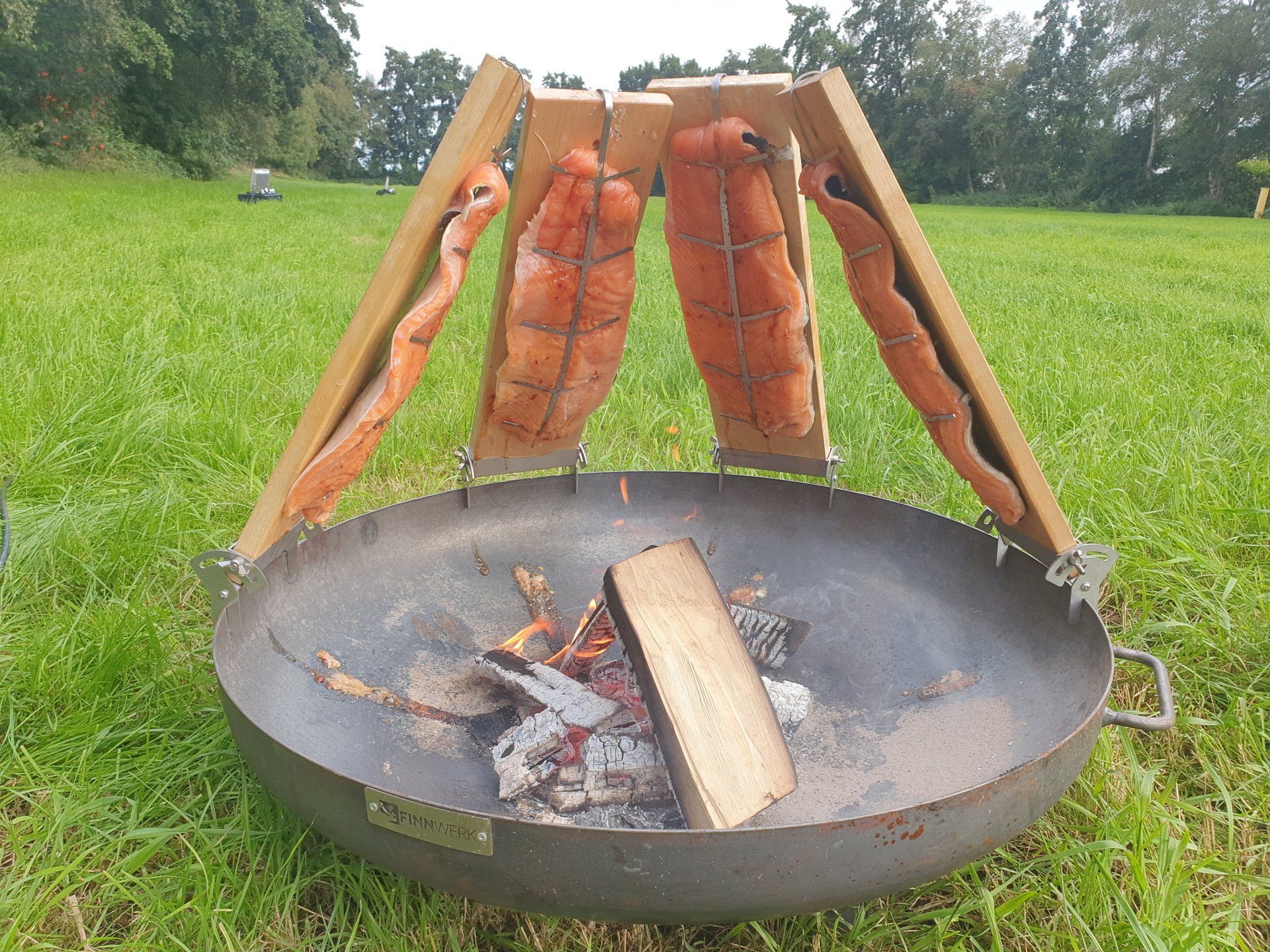 Zalmfilets die boven een vuurkorf op een houten plank langzaam worden gegaard.
