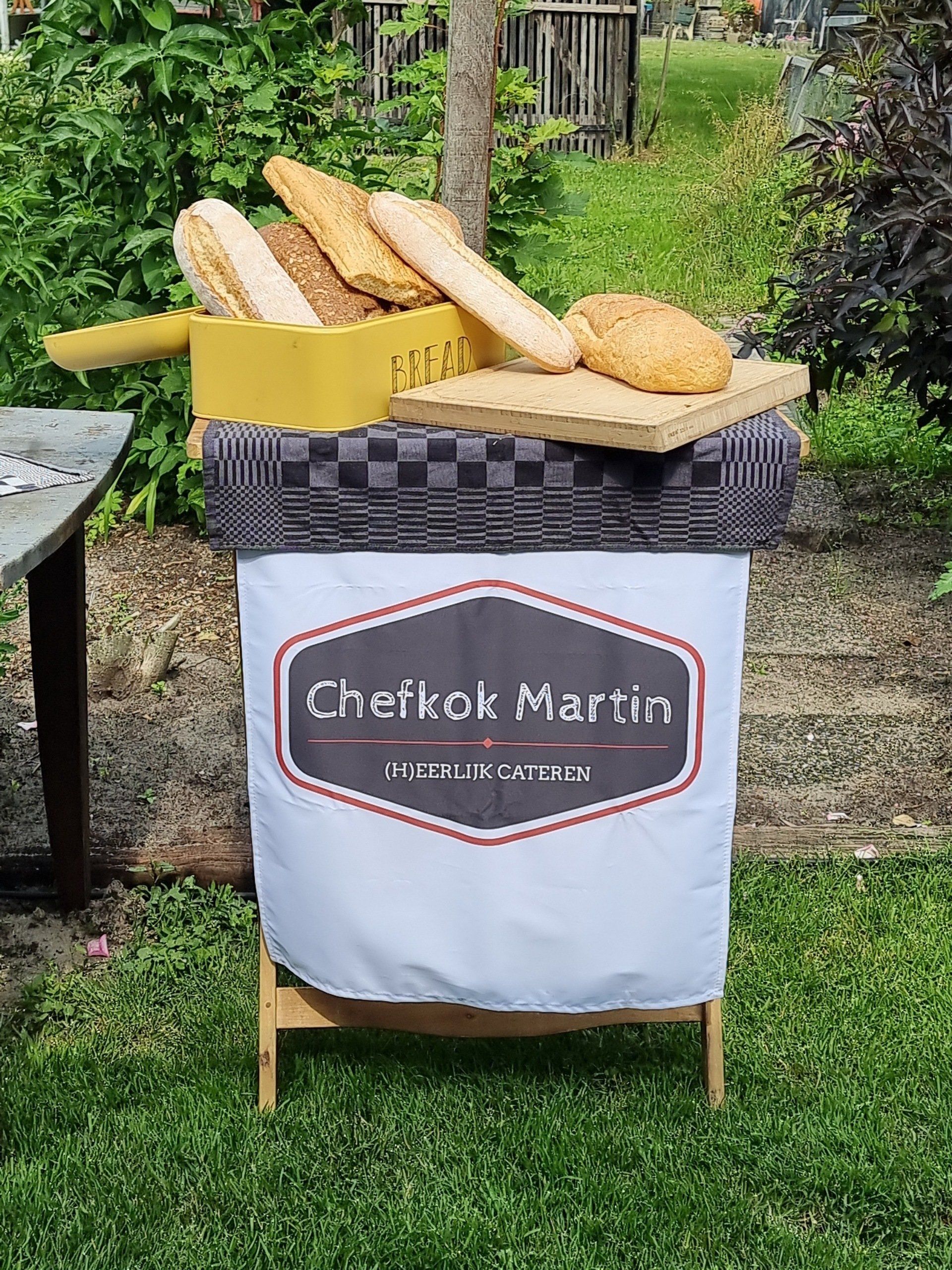 Broodpresentatie van chefkok Martin, met diverse broden in een gele mand, op een geblokte ondergrond, in de buitenlucht.