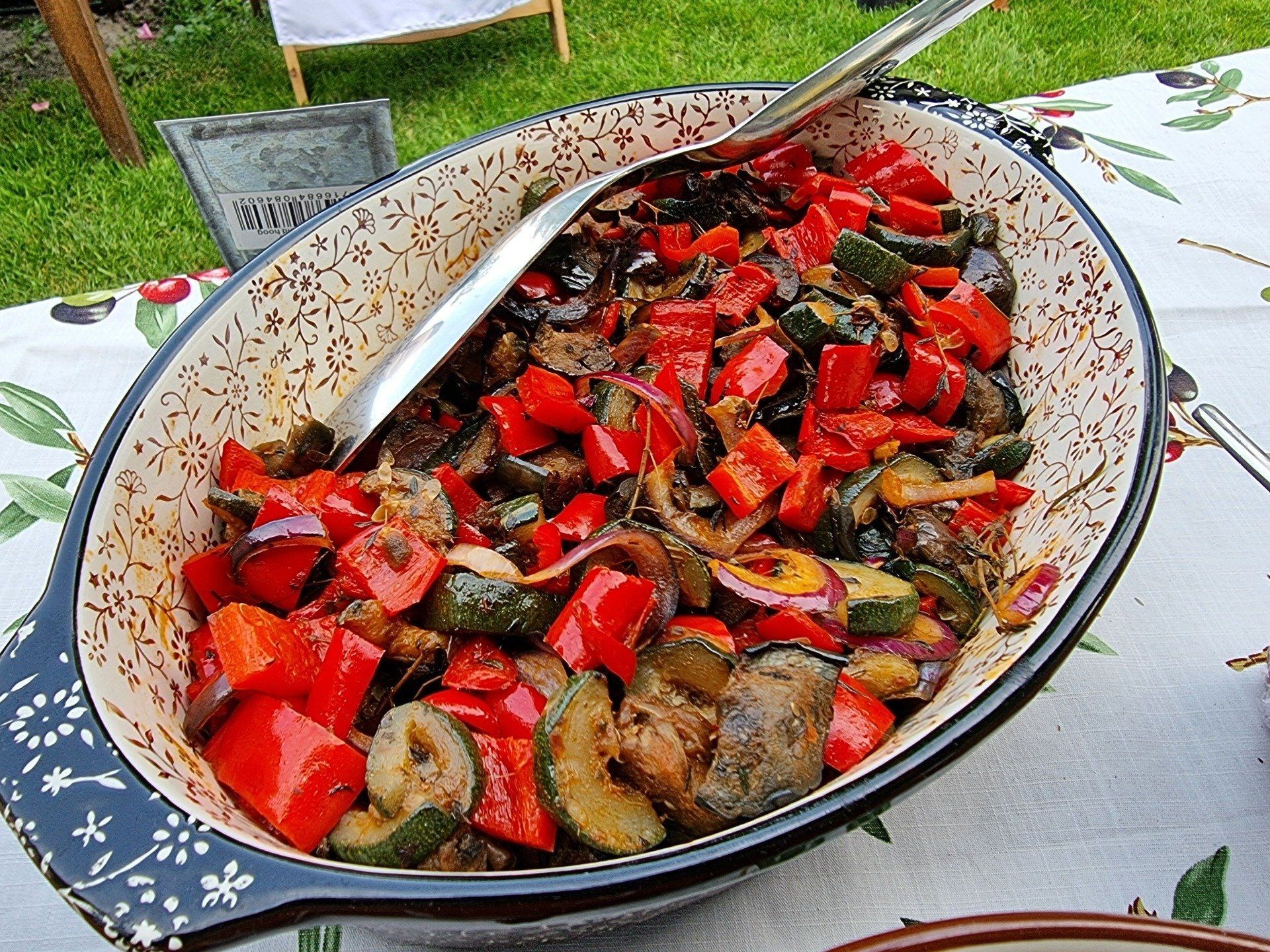 Ovale schaal gevuld met kleurrijke gegrilde groenteratatouille, inclusief serveerlepel.