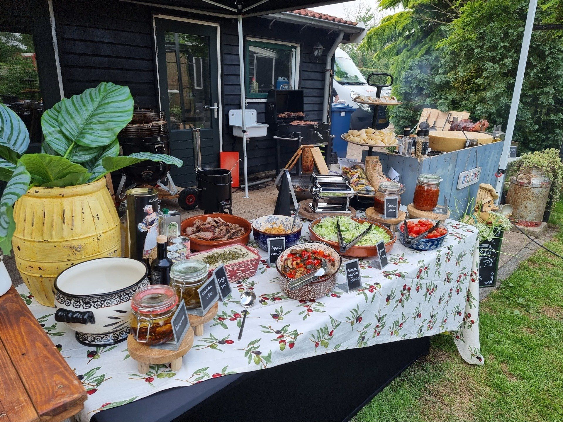 Een buffet in de buitenlucht met diverse gerechten op een tafelkleed met bloemenprint.