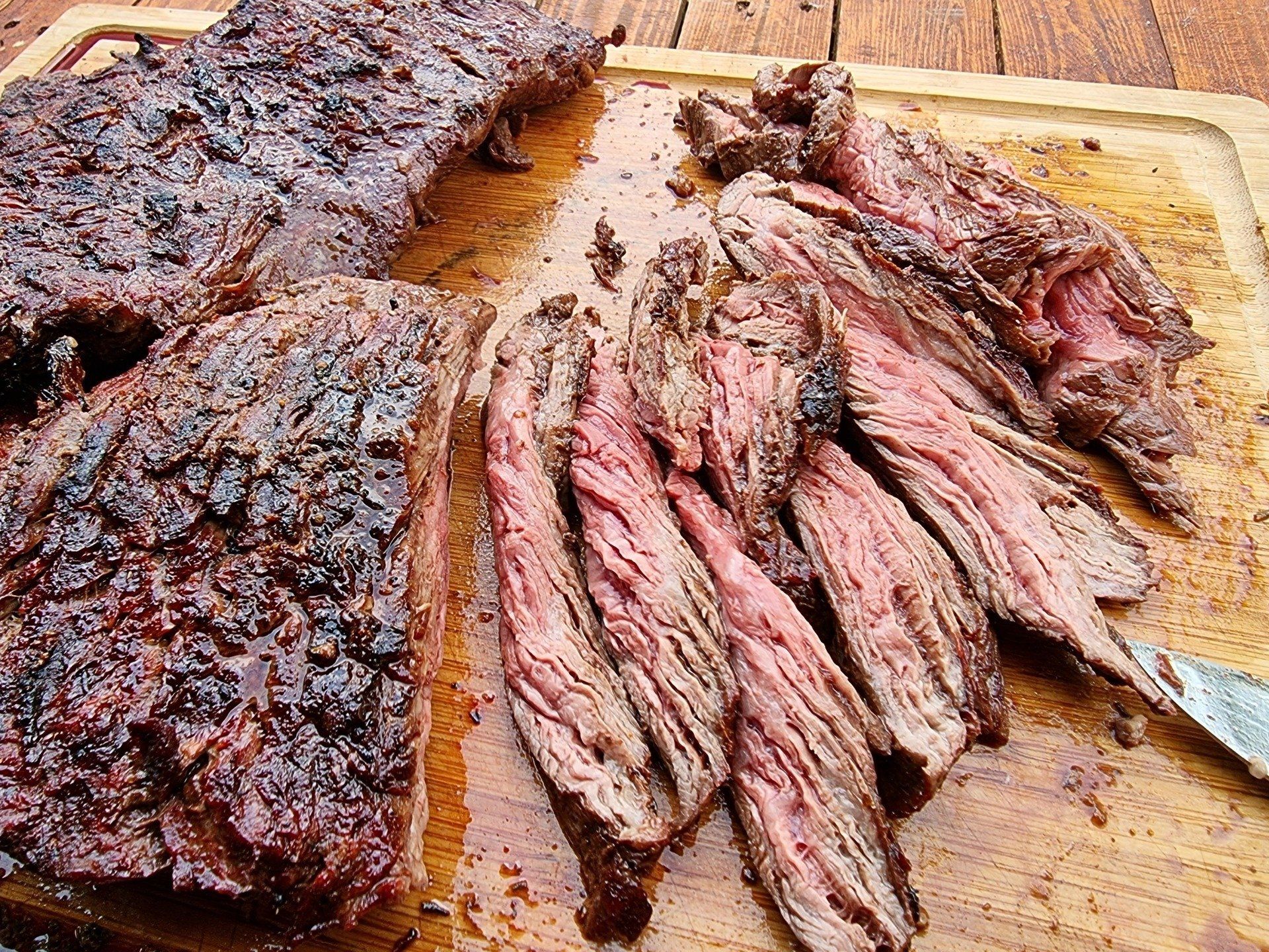 Gegrilde en in plakjes gesneden bavette op een houten snijplank, met een medium-rare binnenkant.
