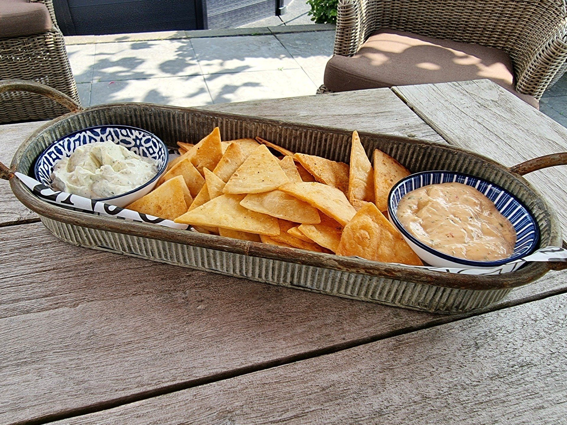 Tortillachips met twee dipsauzen in een decoratieve schaal op een verweerde houten tafel.