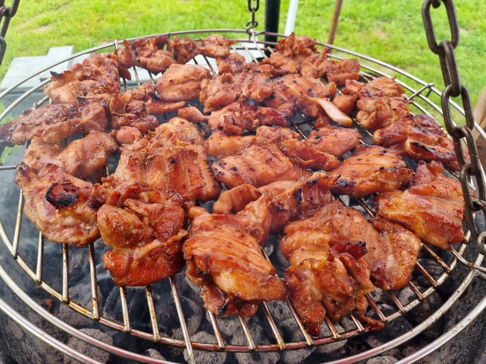 Gegrilde kipstukjes op een ronde, metalen grill boven hete kolen; buitenomgeving.