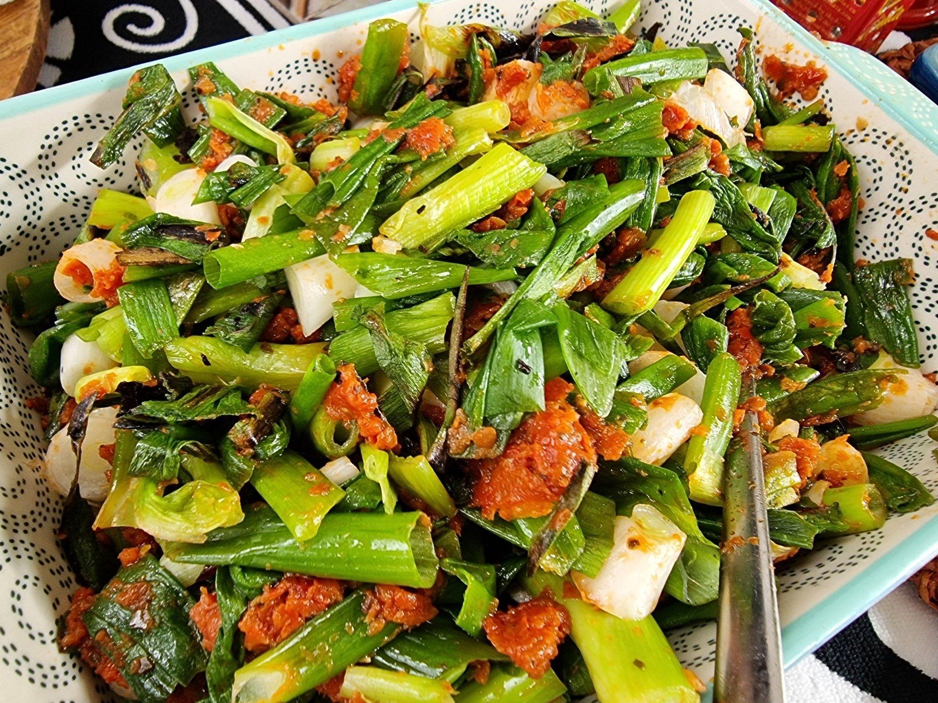 Salade van groene ui met rode specerijen in een wit-blauw gedecoreerd schaaltje.