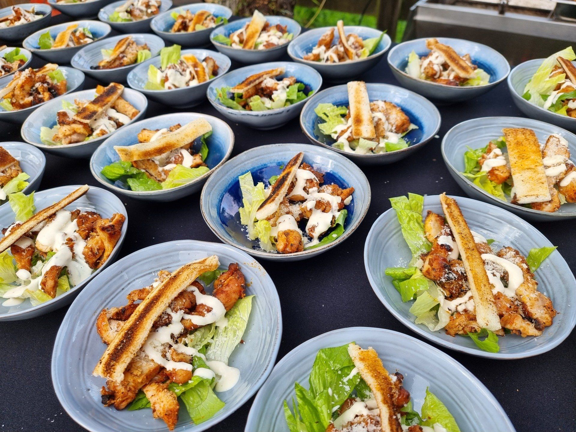 Schalen met salade, gevuld met kip, sla en dressing, klaar om te serveren op een evenement.