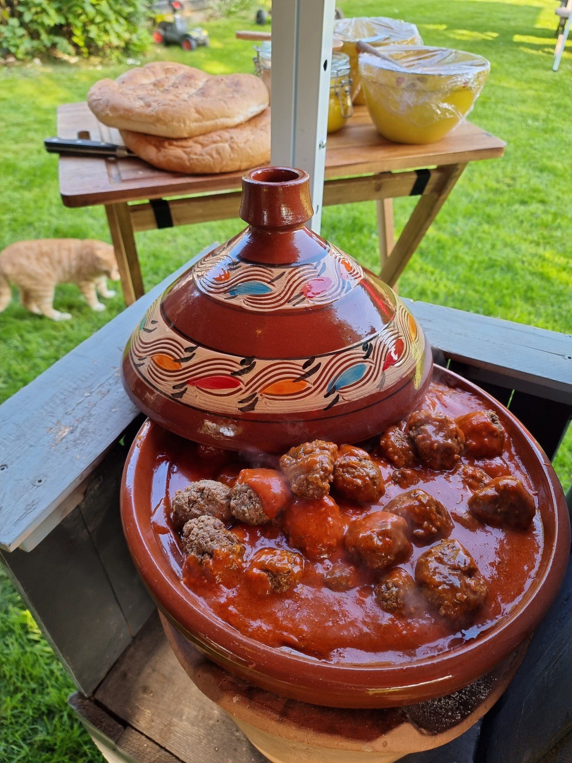 Een Marokkaans tajinegerecht met gehaktballetjes en brood, buiten gegeten; een kat op de achtergrond.