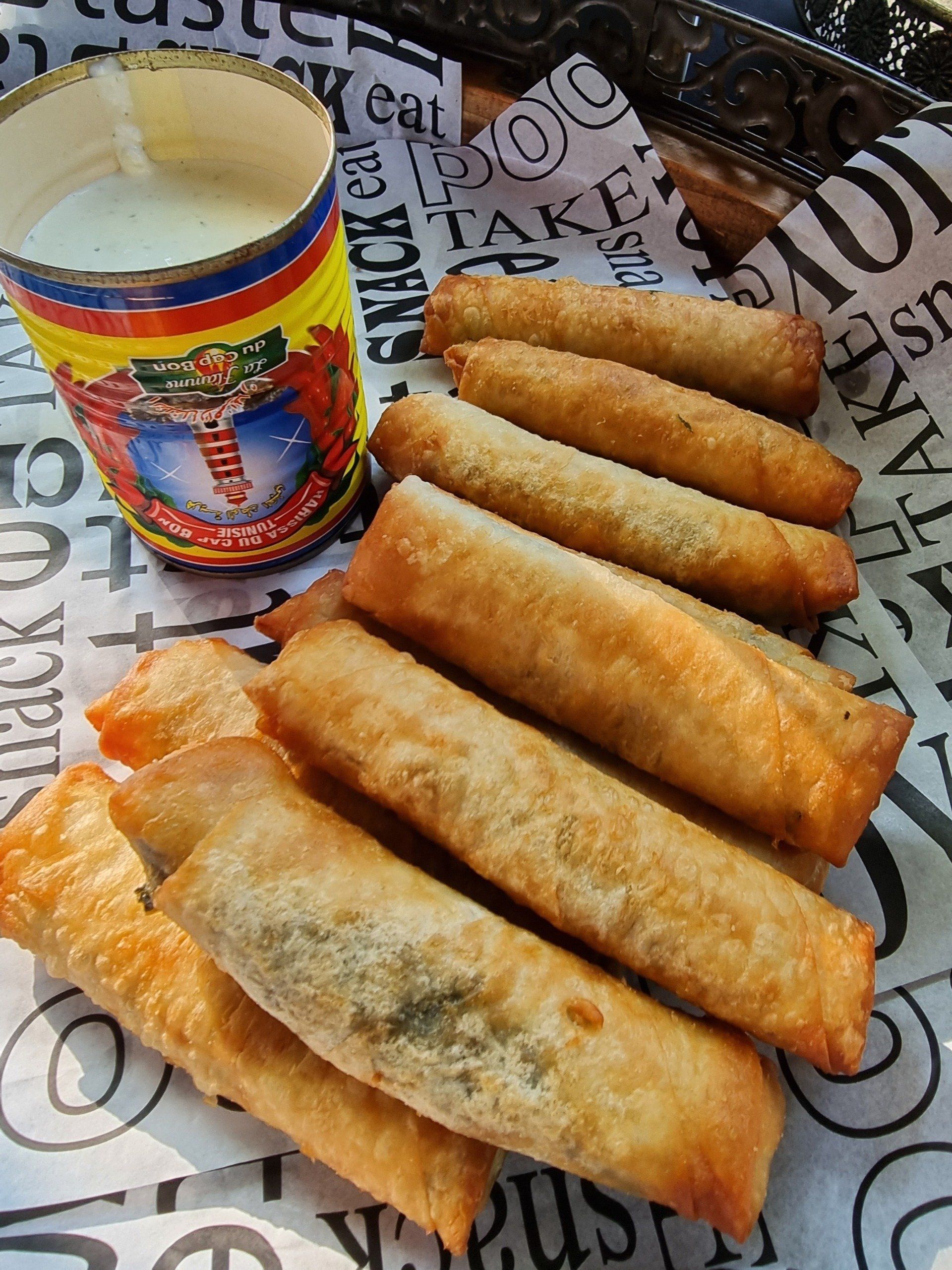 Gefrituurde eetstokjes met dipsaus in een blikje, op bedrukt papier.