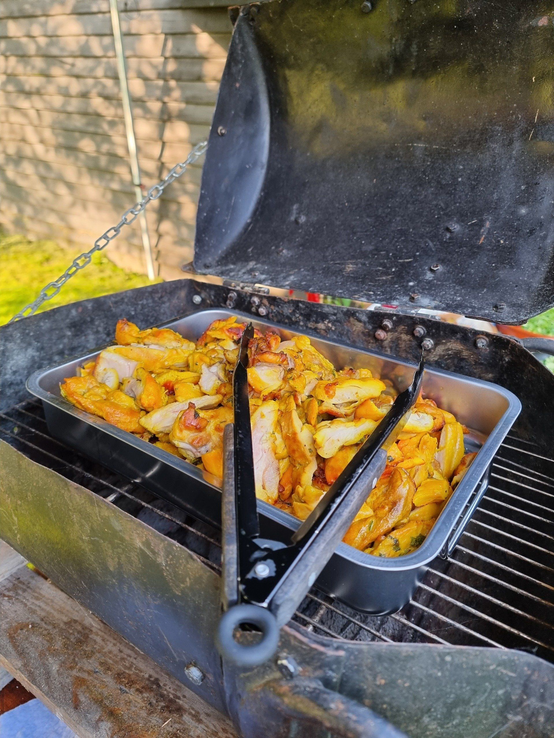 Kippenstukjes die in een bak op de barbecue worden gegrild. 