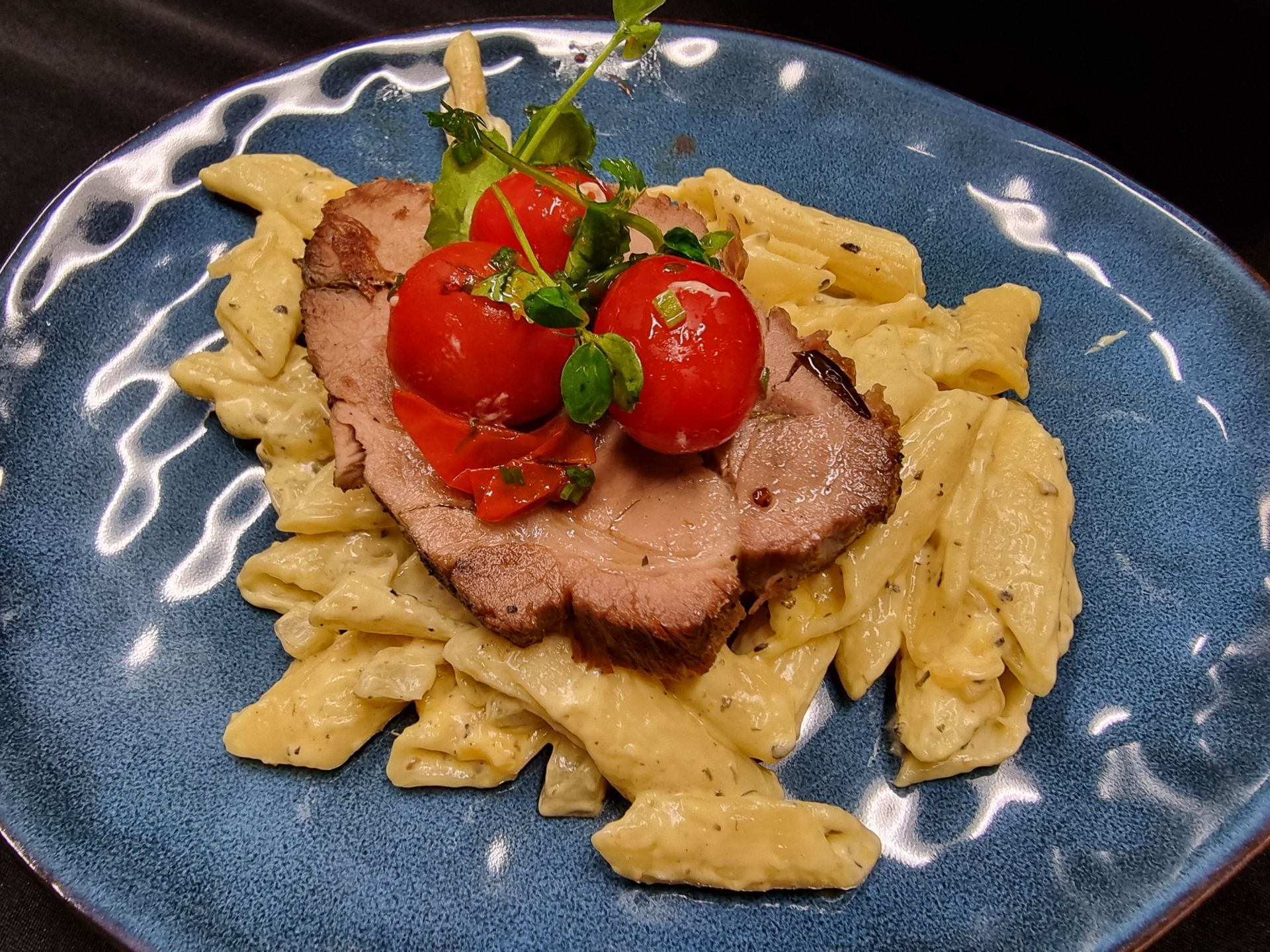 Pastagerecht met plakjes vlees, cherrytomaatjes en kruiden op een blauw bord.
