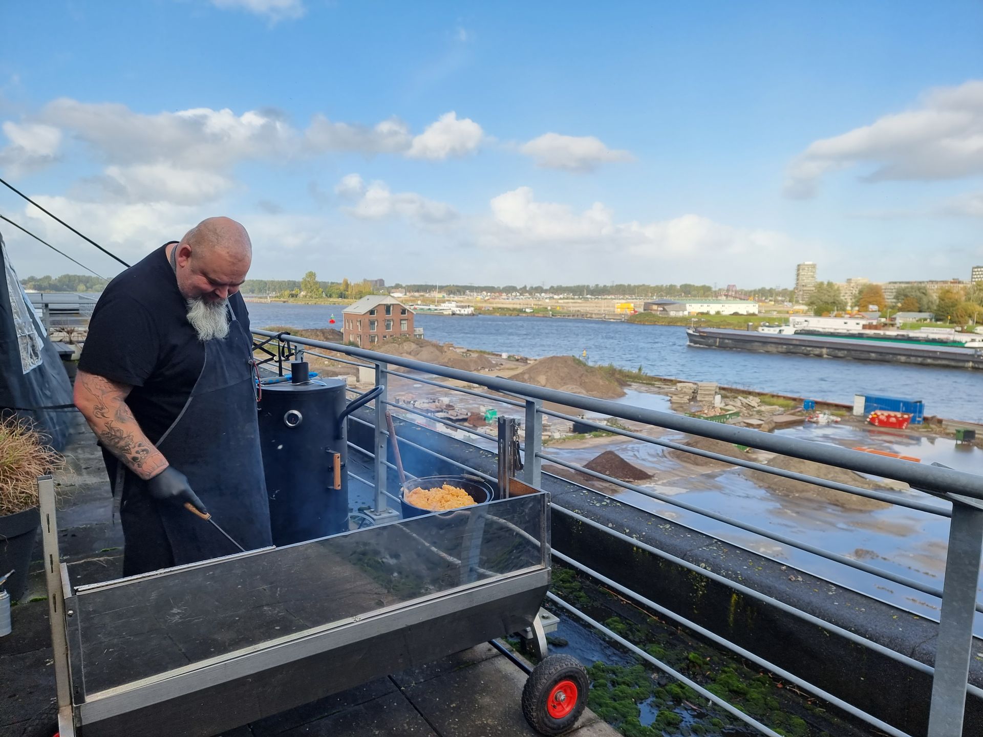 Chefkok Martin staat buiten te grillen op een dakterras in Amsterdam, aan het water. 