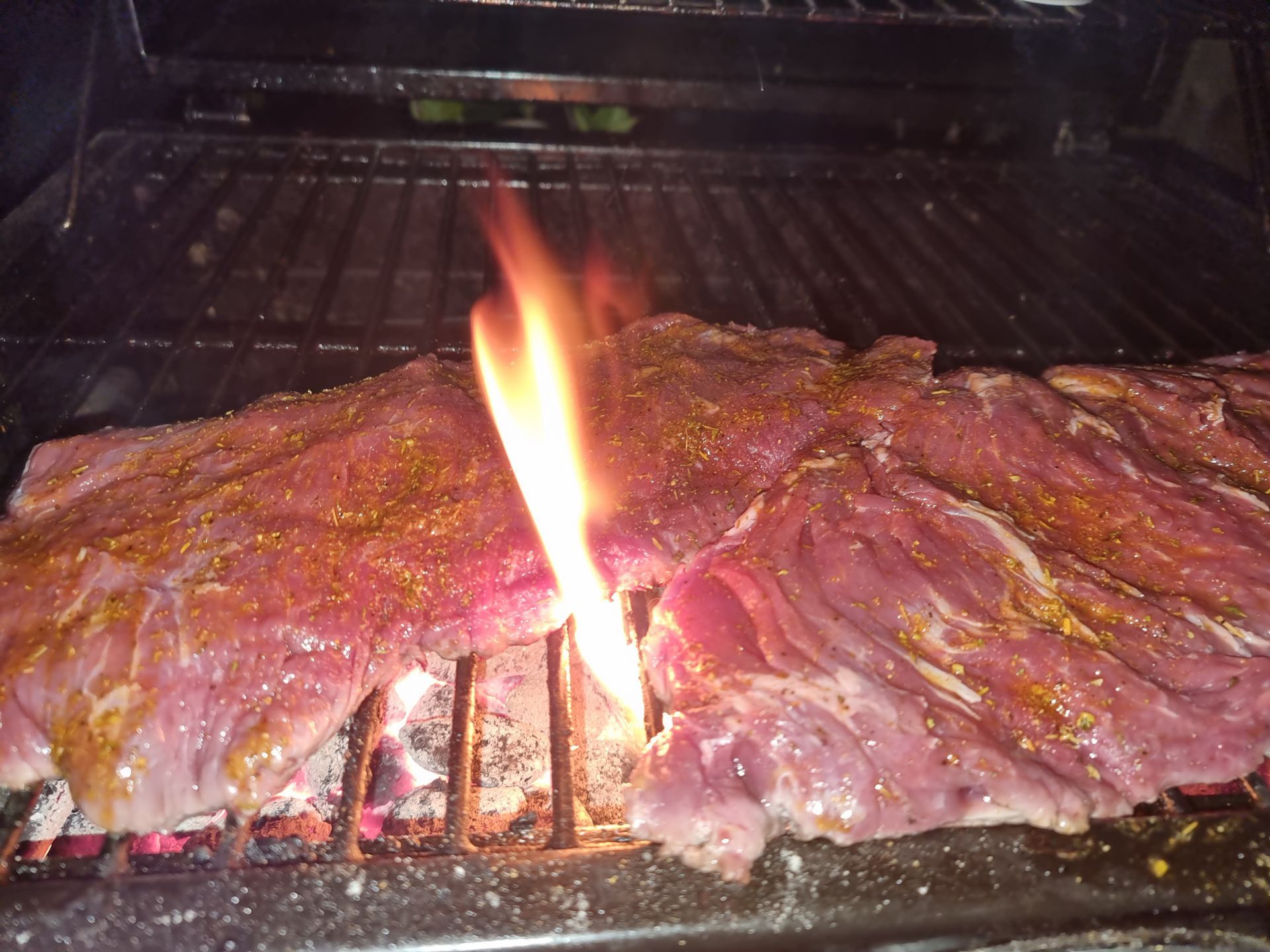 Bavette gekruid op een grill, met vlammen die tussen de roosters opstijgen.