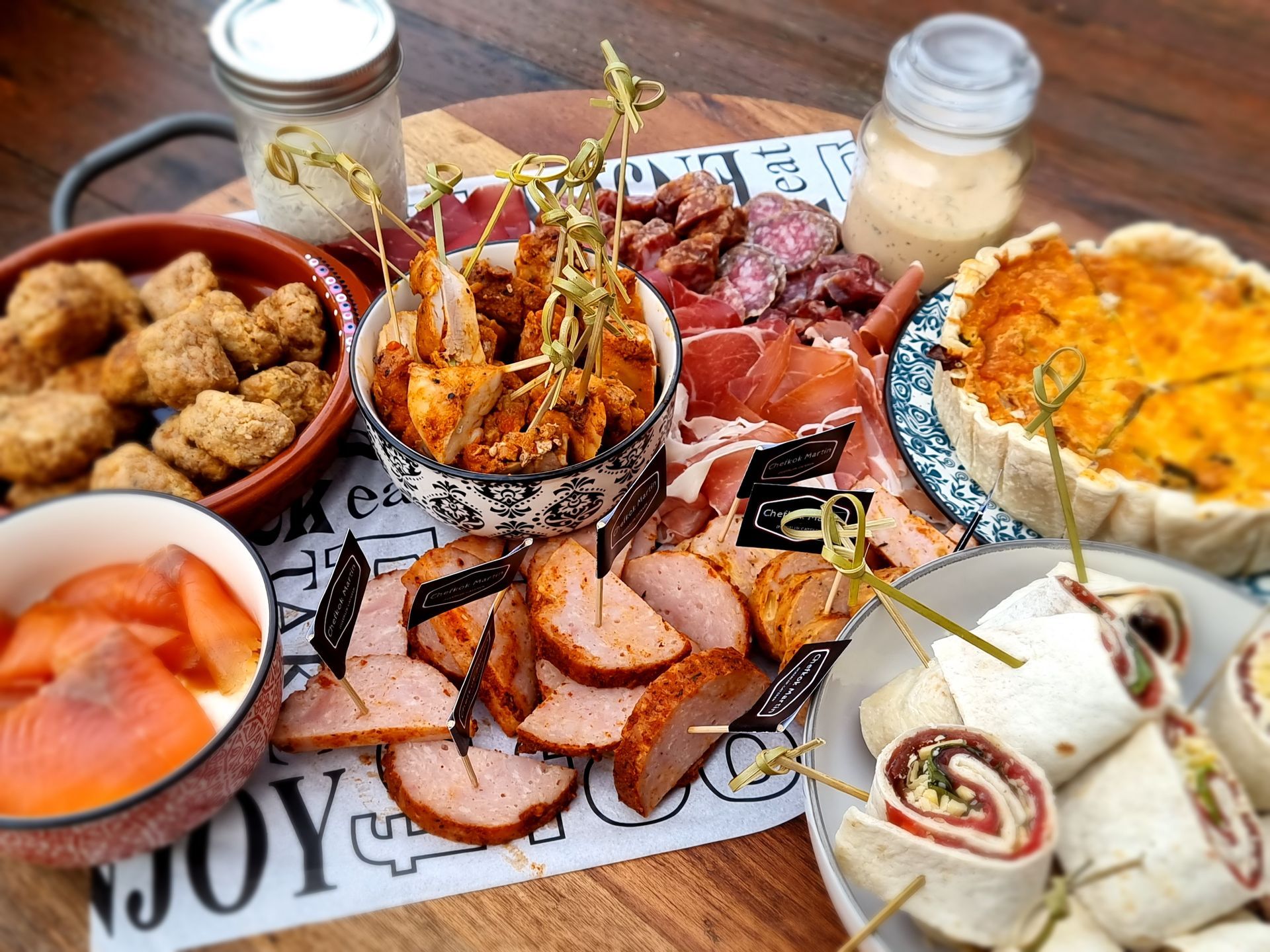 Charcuterieplank met diverse soorten vleeswaren, quiche, gefrituurde hapjes en wraps.