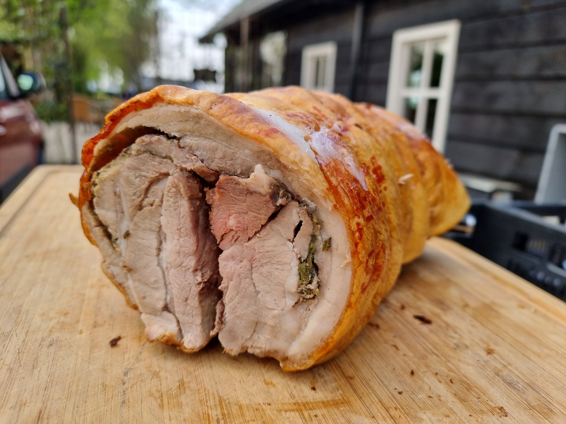 Opgerold varkensgebraad, ingesneden om de binnenkant te onthullen, op een houten snijplank buiten.