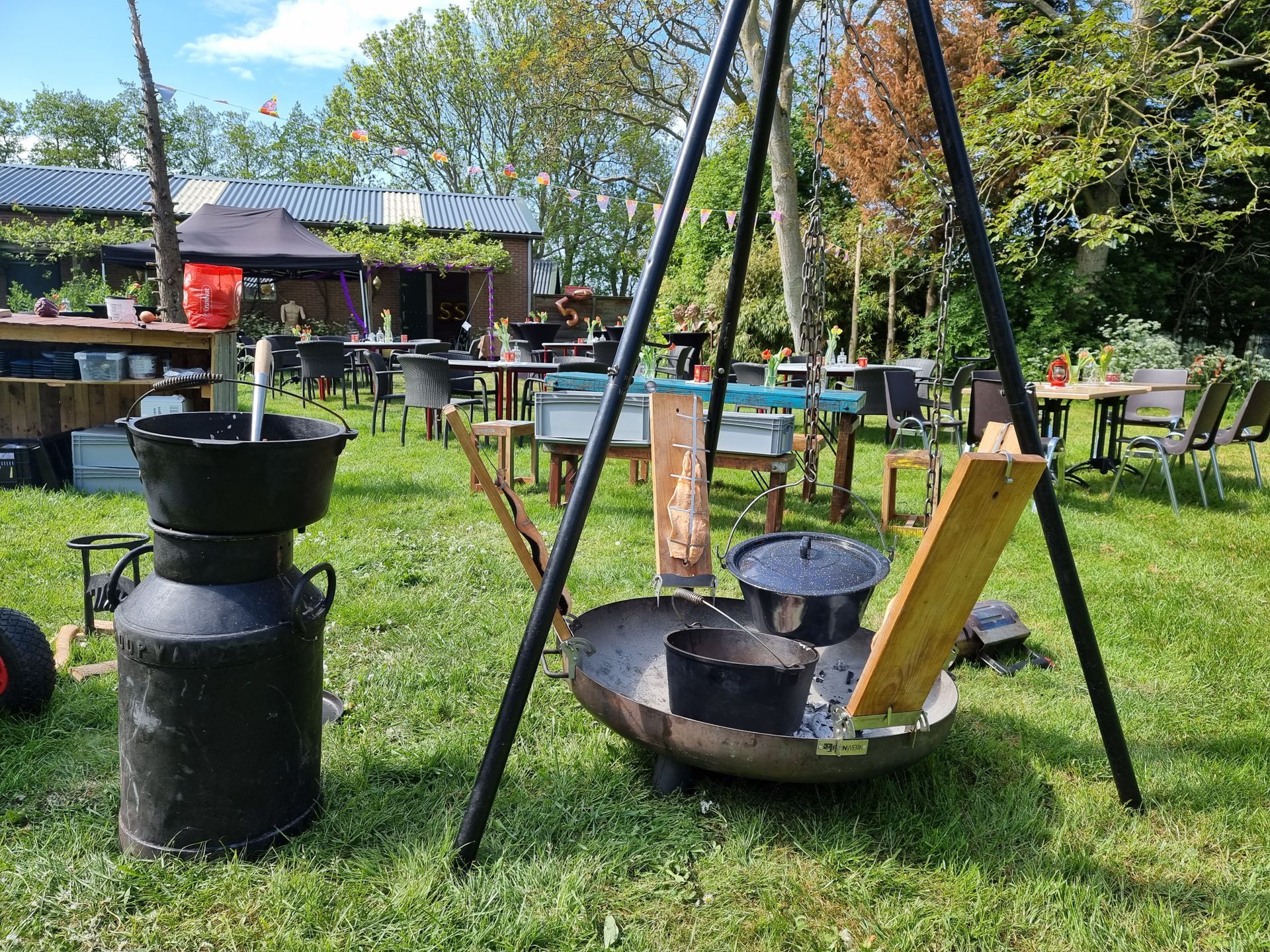 Buitenkeuken met statief boven een vuurplaats, pannen en tafels in de tuin van Hofstede Lust en Last.