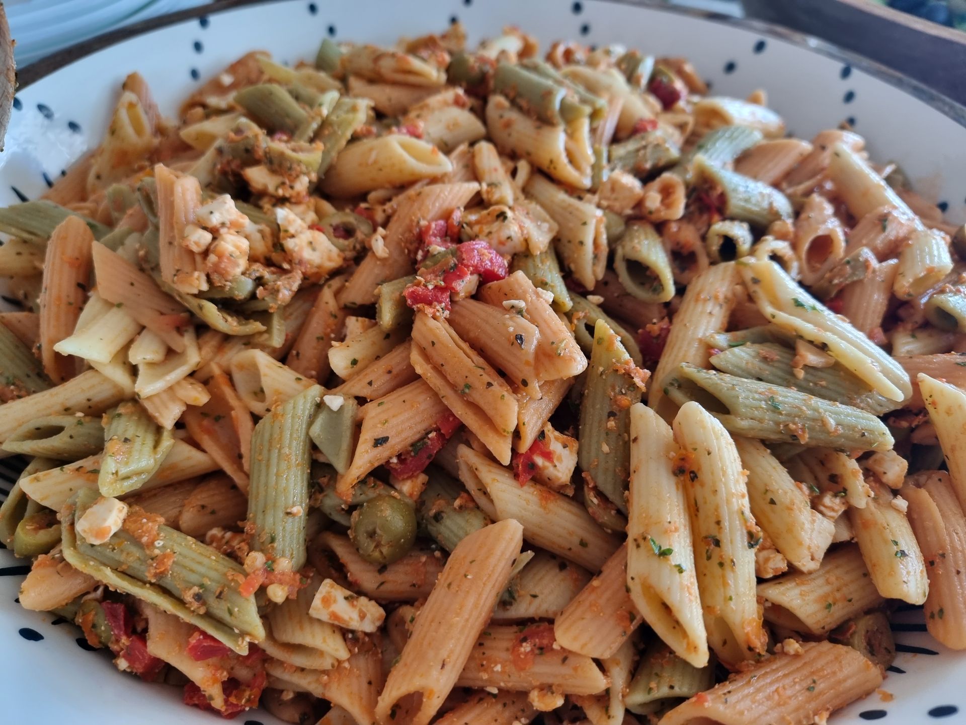 Pastasalade in een kom, met driekleurige penne, saus en verkruimelde kaas.
