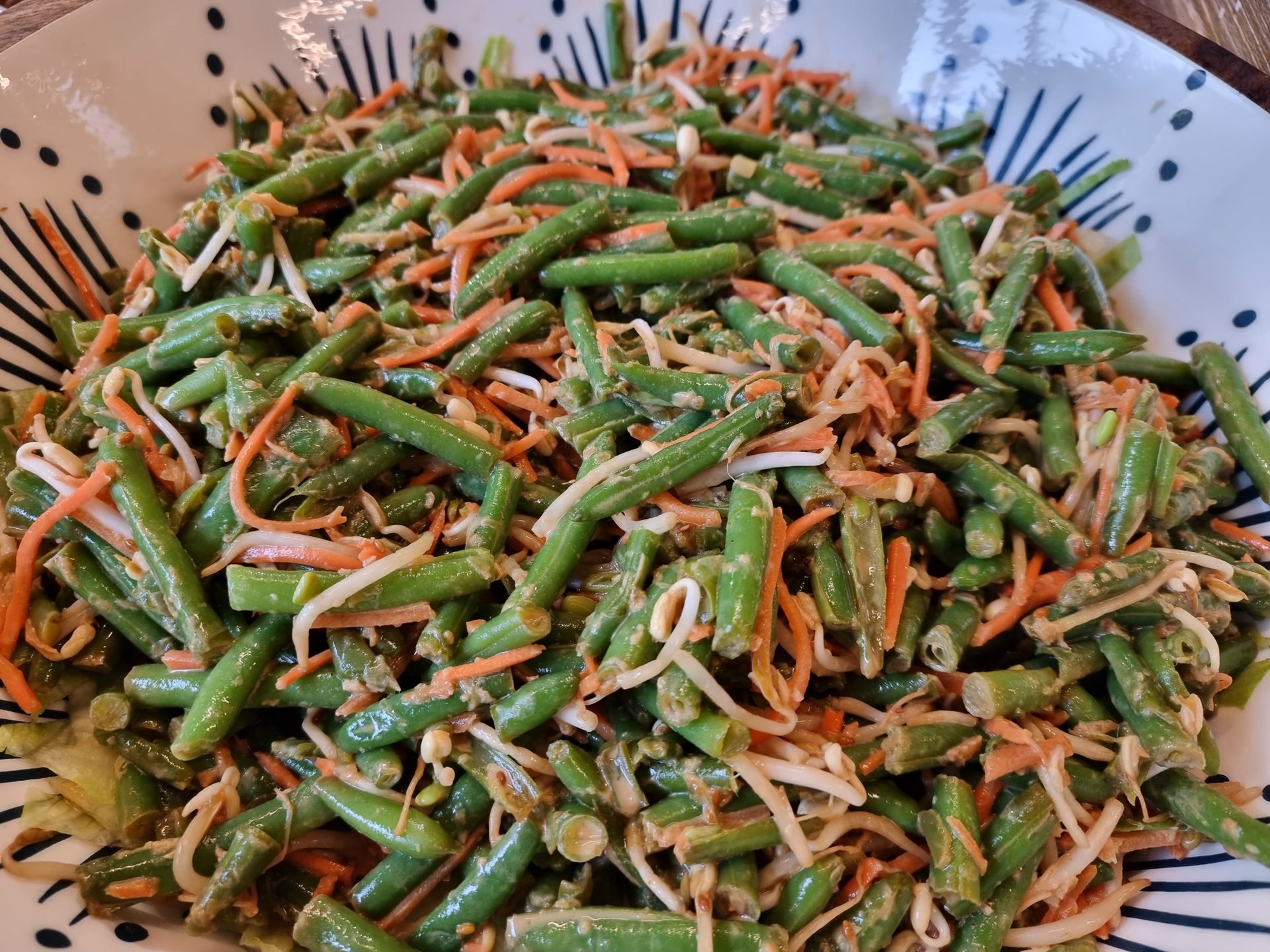 Salade van sperziebonen, wortels en taugé in een kom.