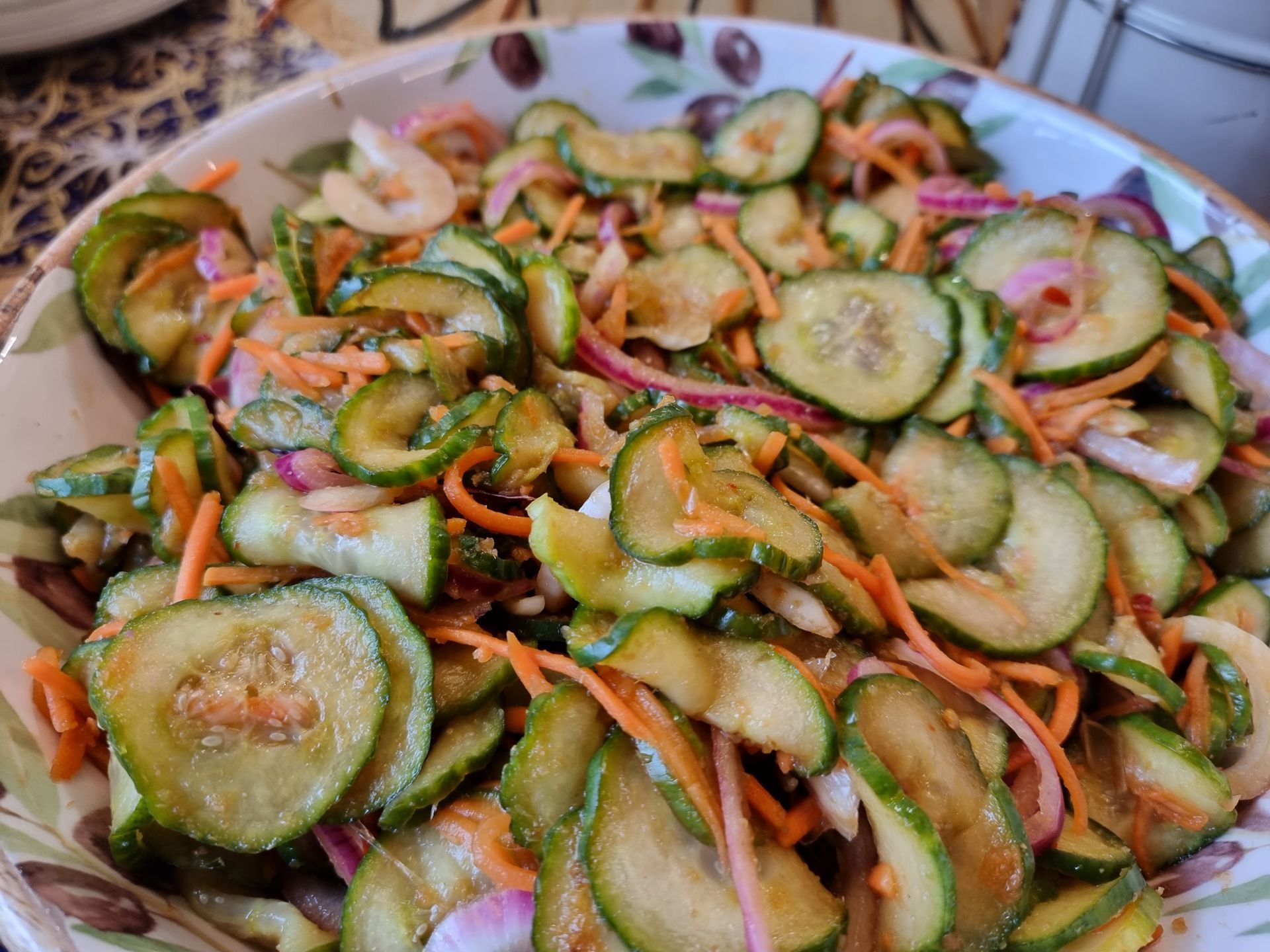 Komkommersalade met plakjes komkommer, rode ui en wortel in een decoratieve kom.