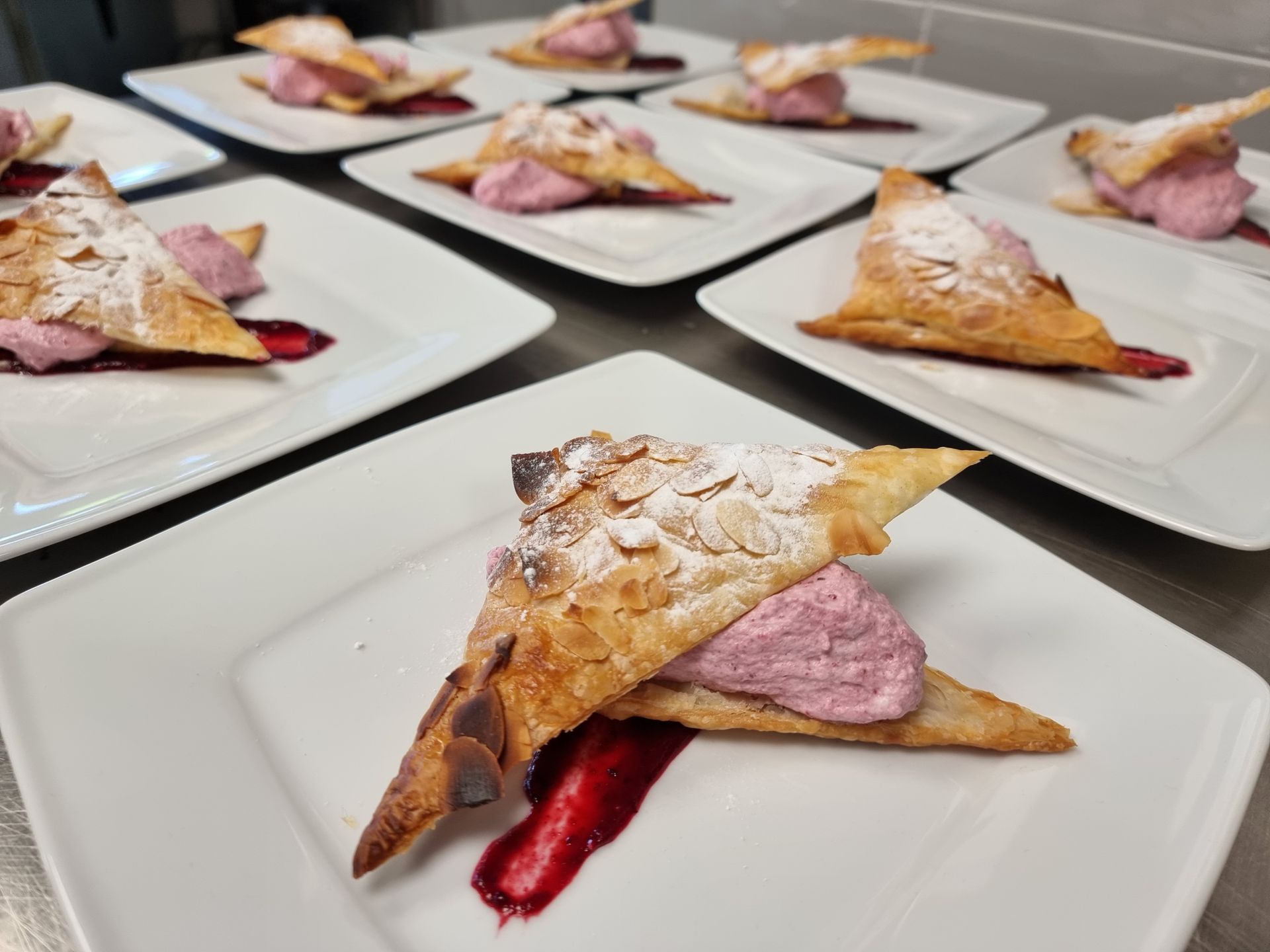 Borden met gebakjes met roze vulling en saus, bestrooid met poedersuiker, staan ​​uitgestald op een oppervlak.