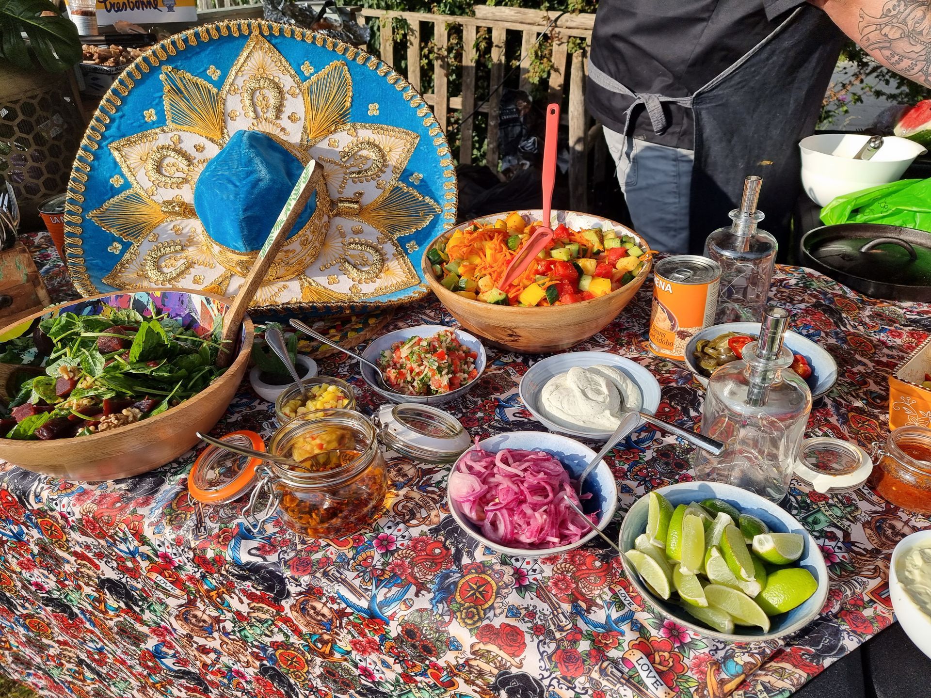 Een kleurrijk uitgestald Mexicaans buffet: salades, salsa's, sauzen, limoenen en een sombrero op een kleurrijke tafel.