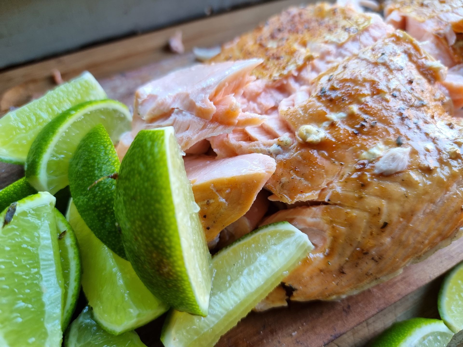 Warm gerookte zalm met limoenpartjes op een houten plank.