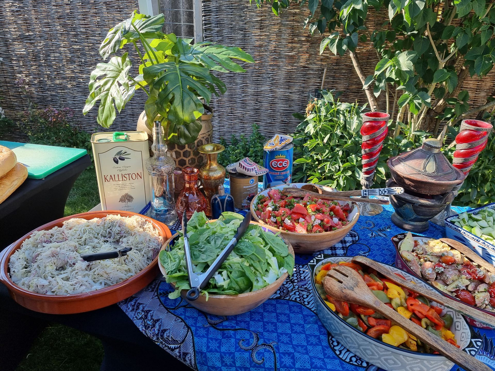 Buffettafel met diverse salades en bijgerechten in de buitenlucht, met decoratief glaswerk.