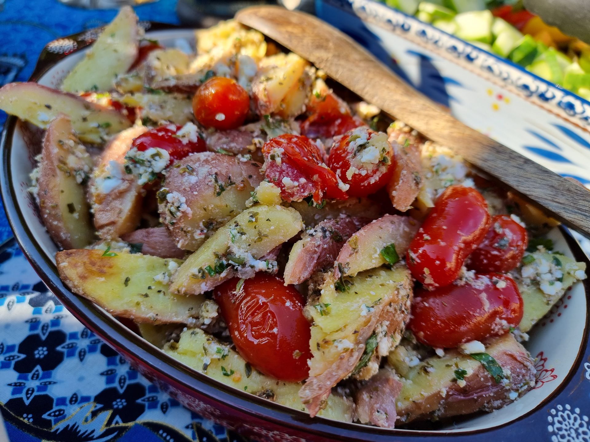 Aardappelsalade met rode tomaten in een keramische kom, met houten lepel.