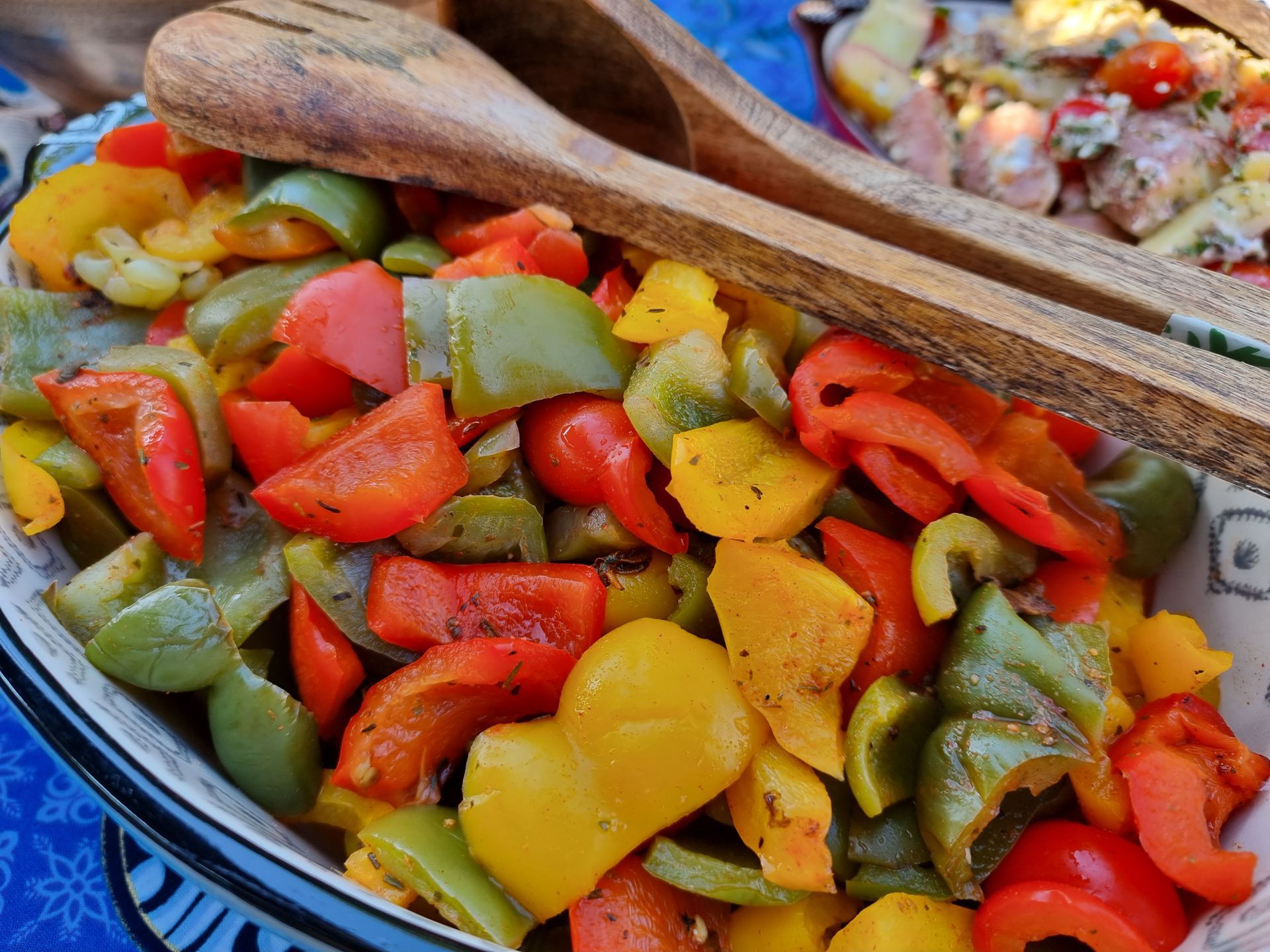 Kleurrijk geroosterde paprika's in een serveerschaal met houten lepels.