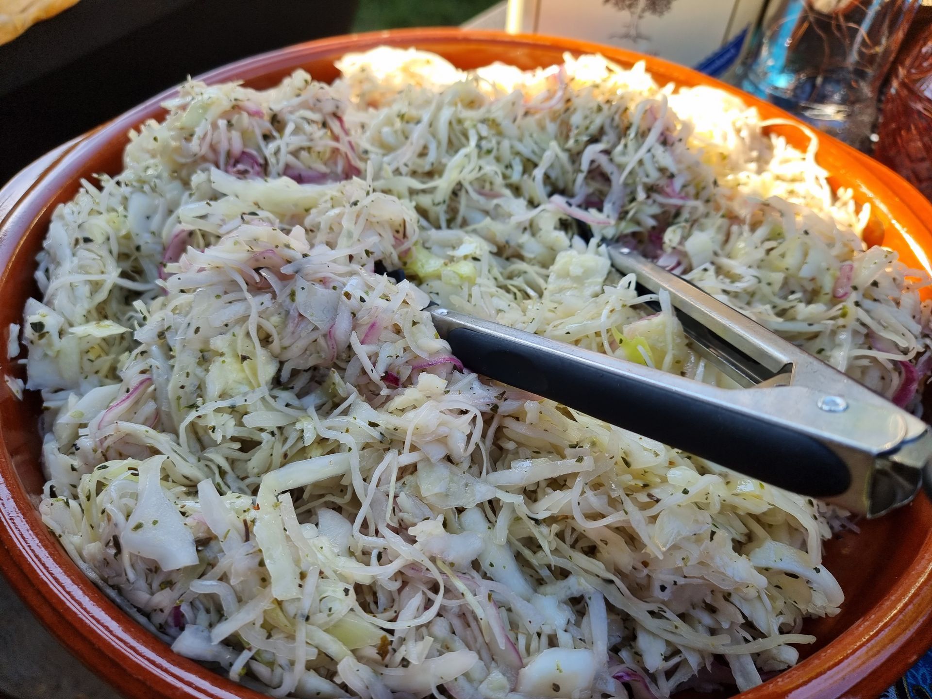 Gesneden koolsalade in een bruine kom, tang om te serveren.