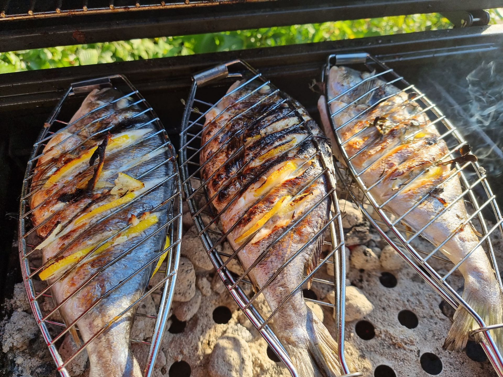 Drie hele vissen, veilig opgeborgen in draadmandjes, worden gegrild op een houtskoolgrill.