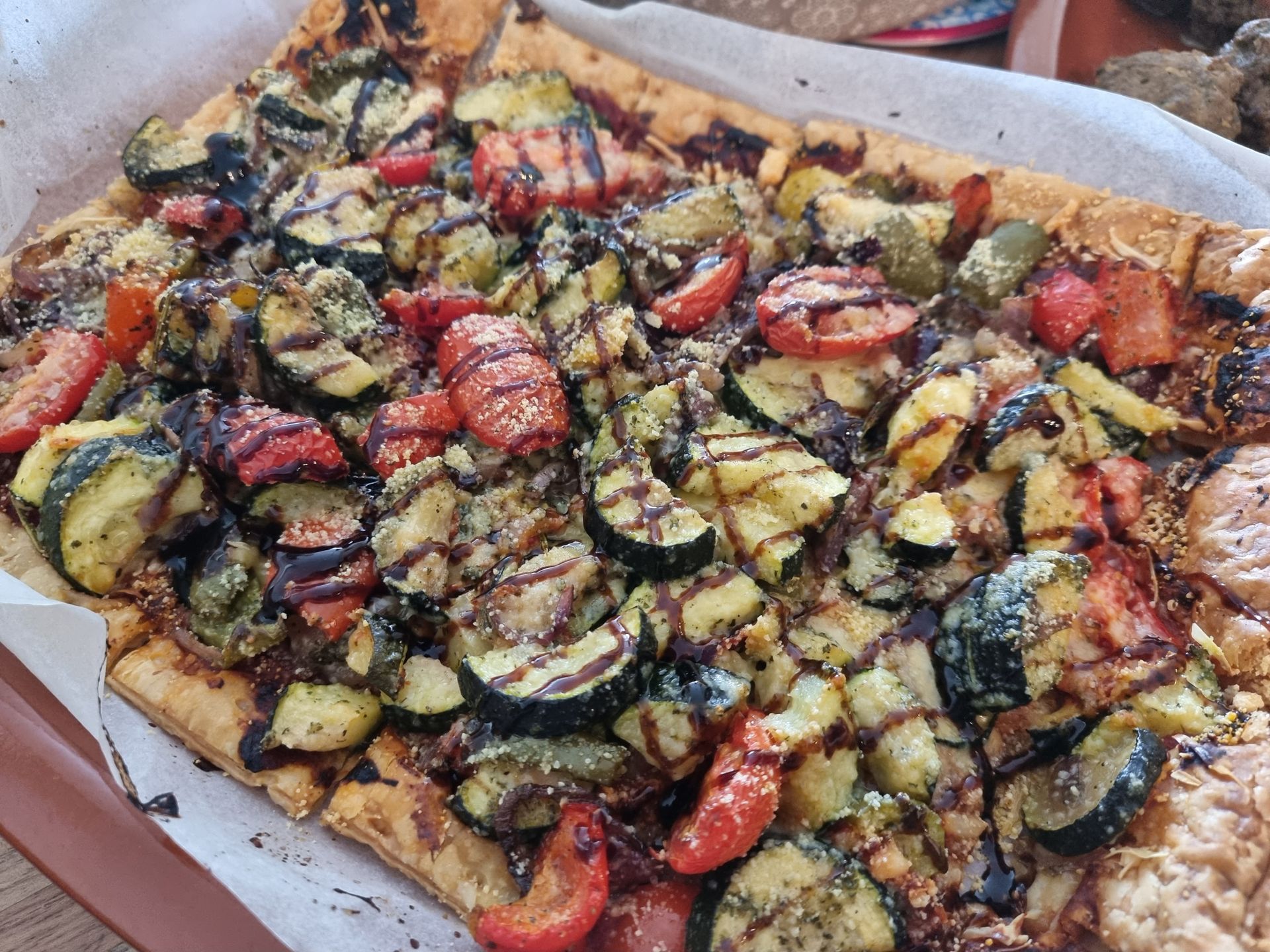Groentetaart met gegrilde courgette, tomaten en balsamico glazuur op een rechthoekige deegbodem.