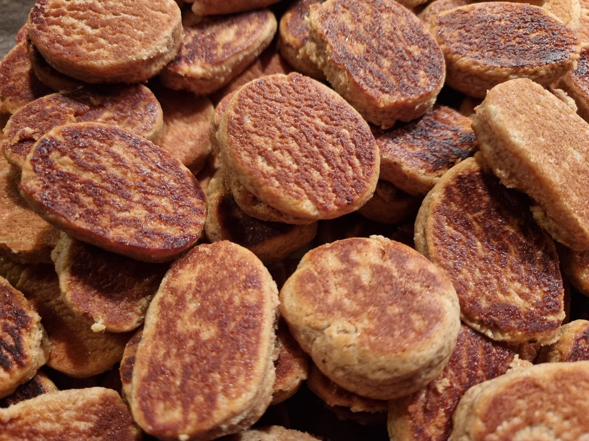 Close-up van een stapel kleine, ronde, goudbruine koekjes met een gestructureerd oppervlak.