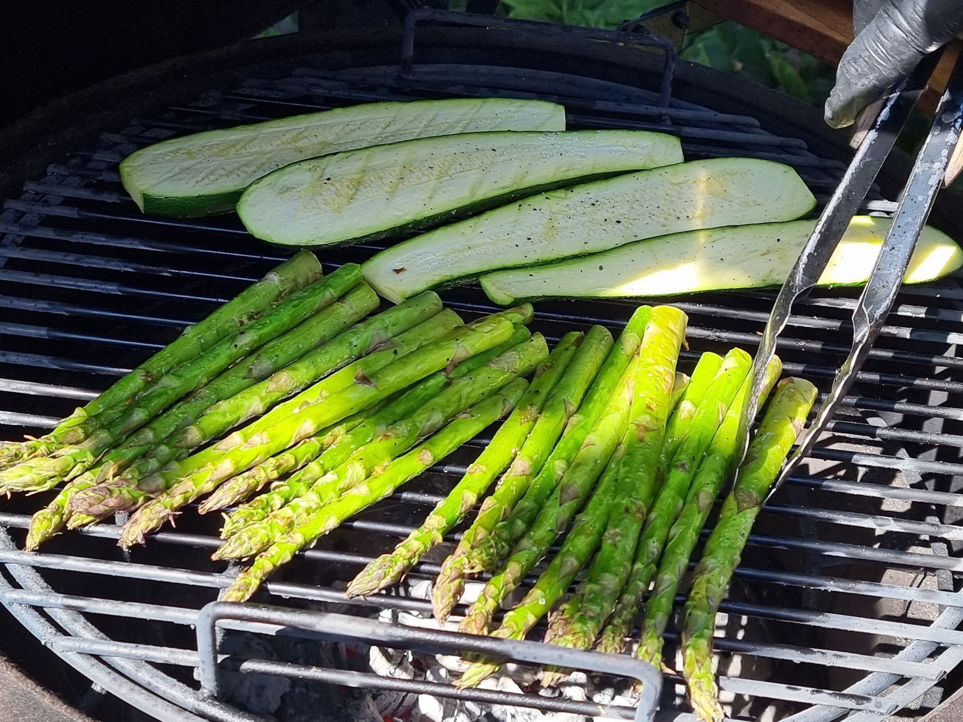 Gegrilde courgette en asperges op een houtskoolgrill. Tang in beeld.