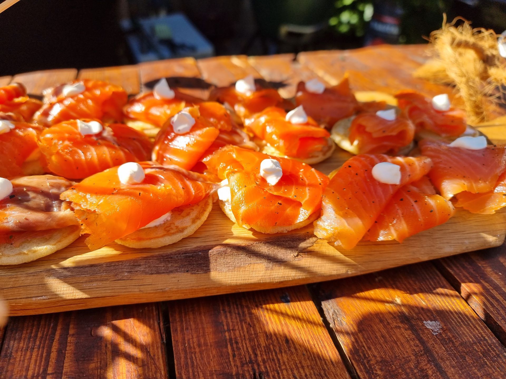 Hapjes met gerookte zalm op een houten plank, gegarneerd met room en kruiden.