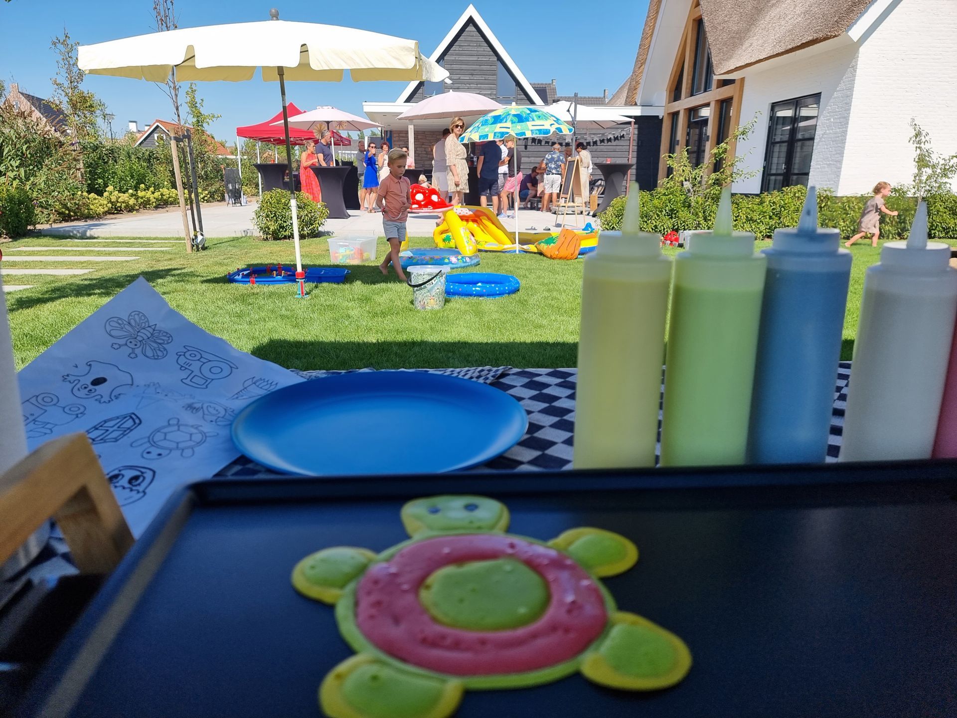 Een pancake-art bar met kleurrijke beslagflesjes, een schildpadpannenkoek en een blauw bord.