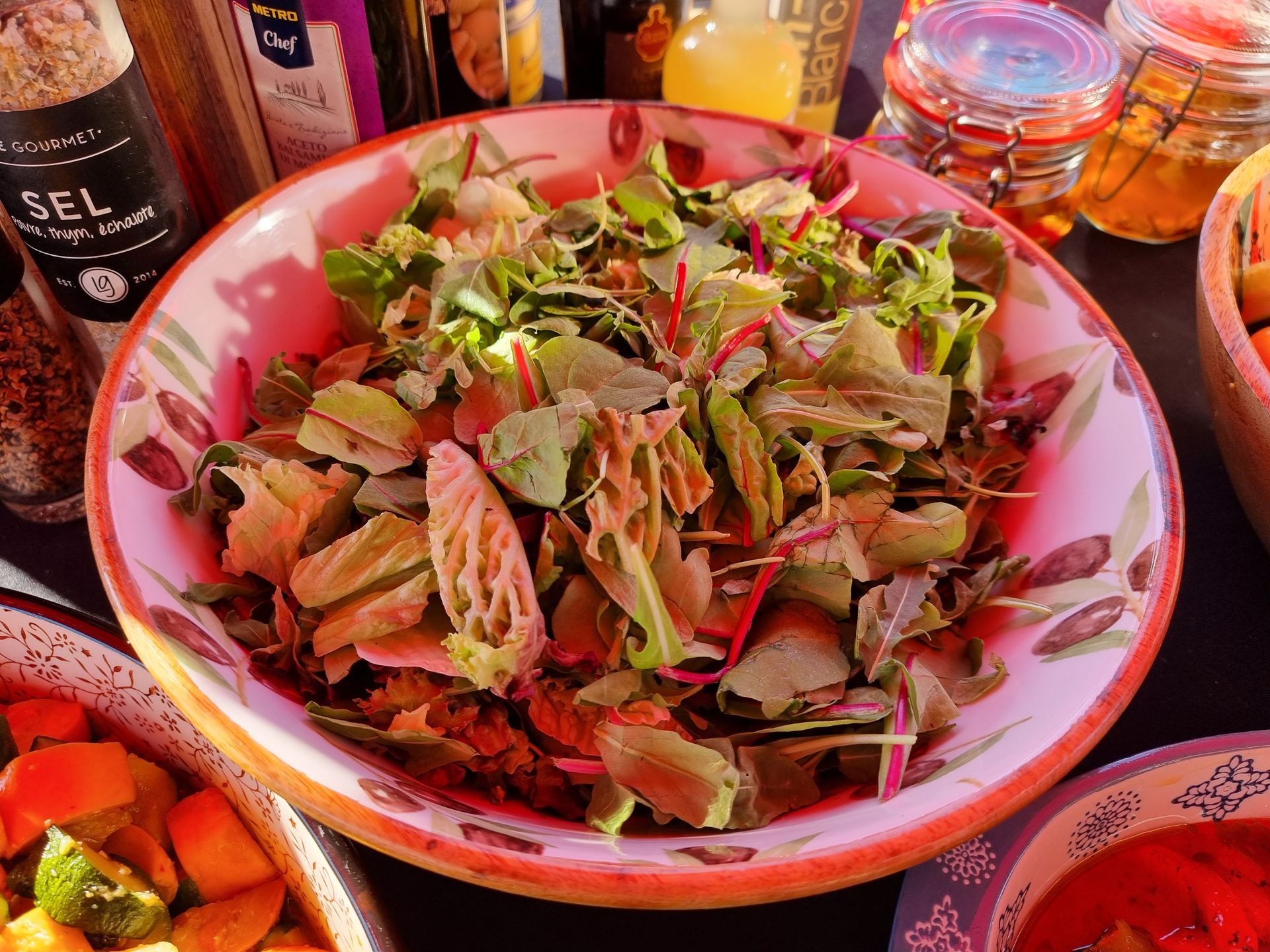 Salade in een decoratieve kom met andere etenswaren op de achtergrond.
