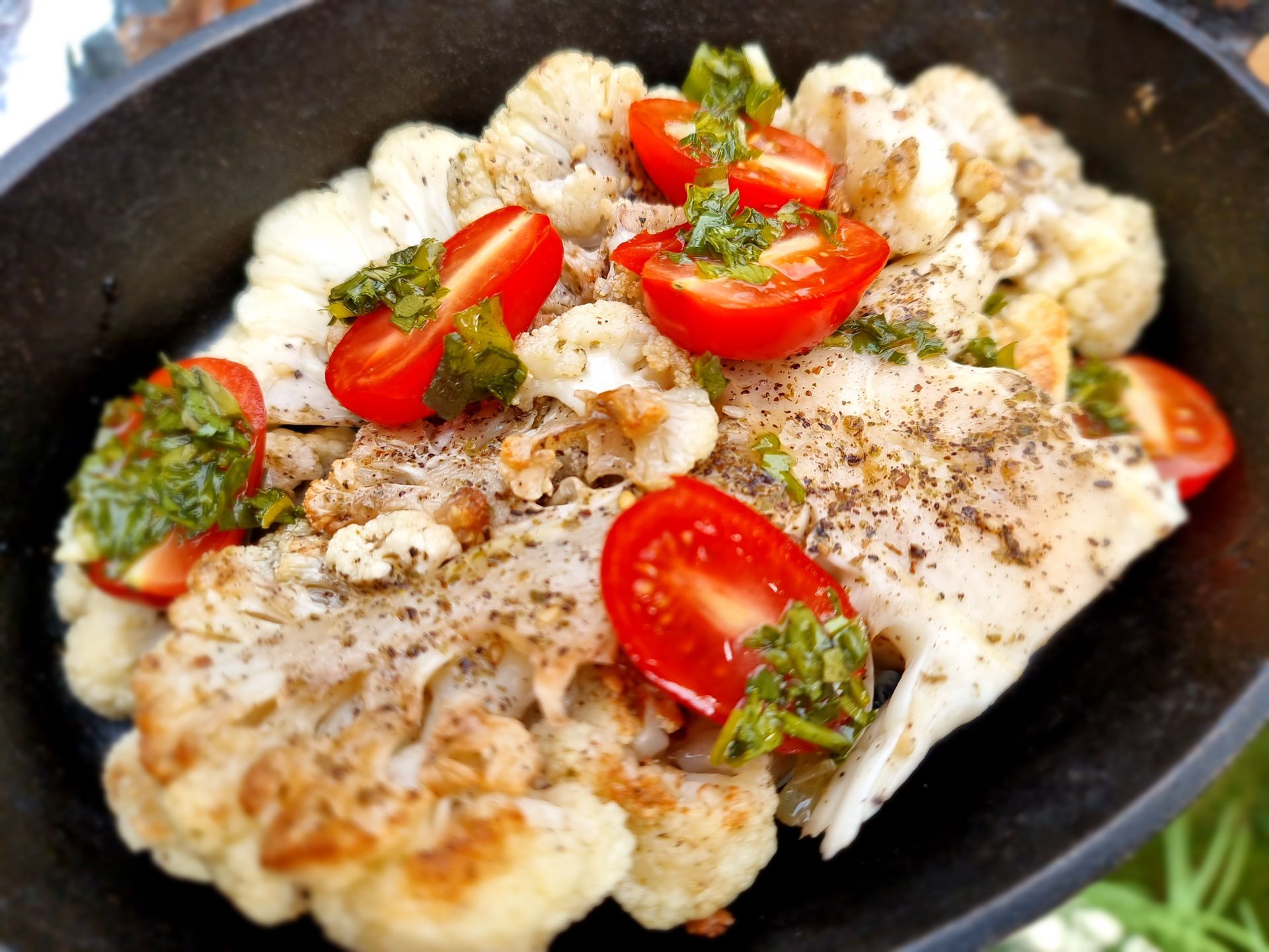 Geroosterde bloemkoolsteak met pesto en tomaten, gebakken in een zwarte pan.