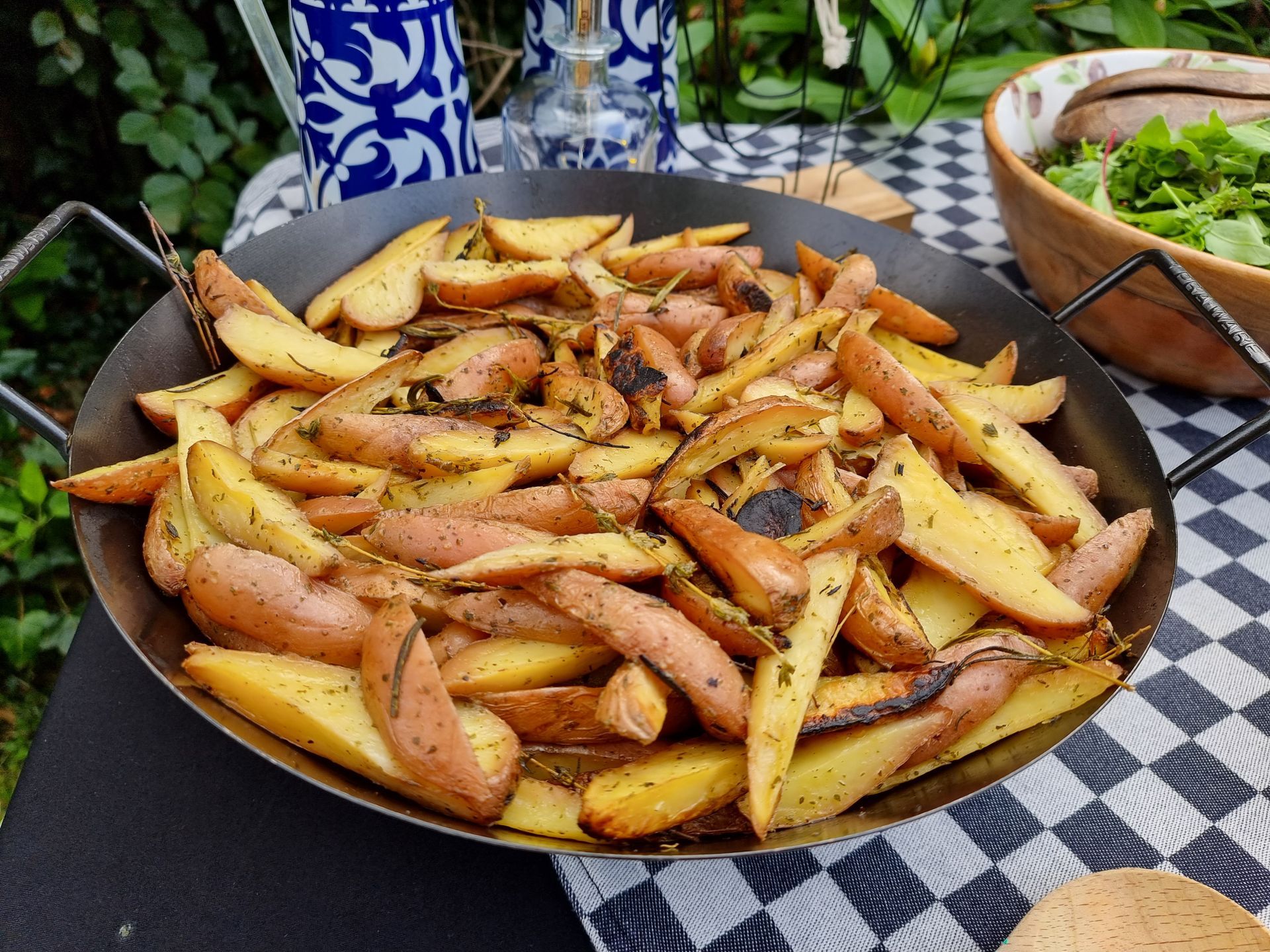 Geroosterde rozeval aardappelpartjes in een zwarte pan, op een geruite tafel, tussen sla en planten.