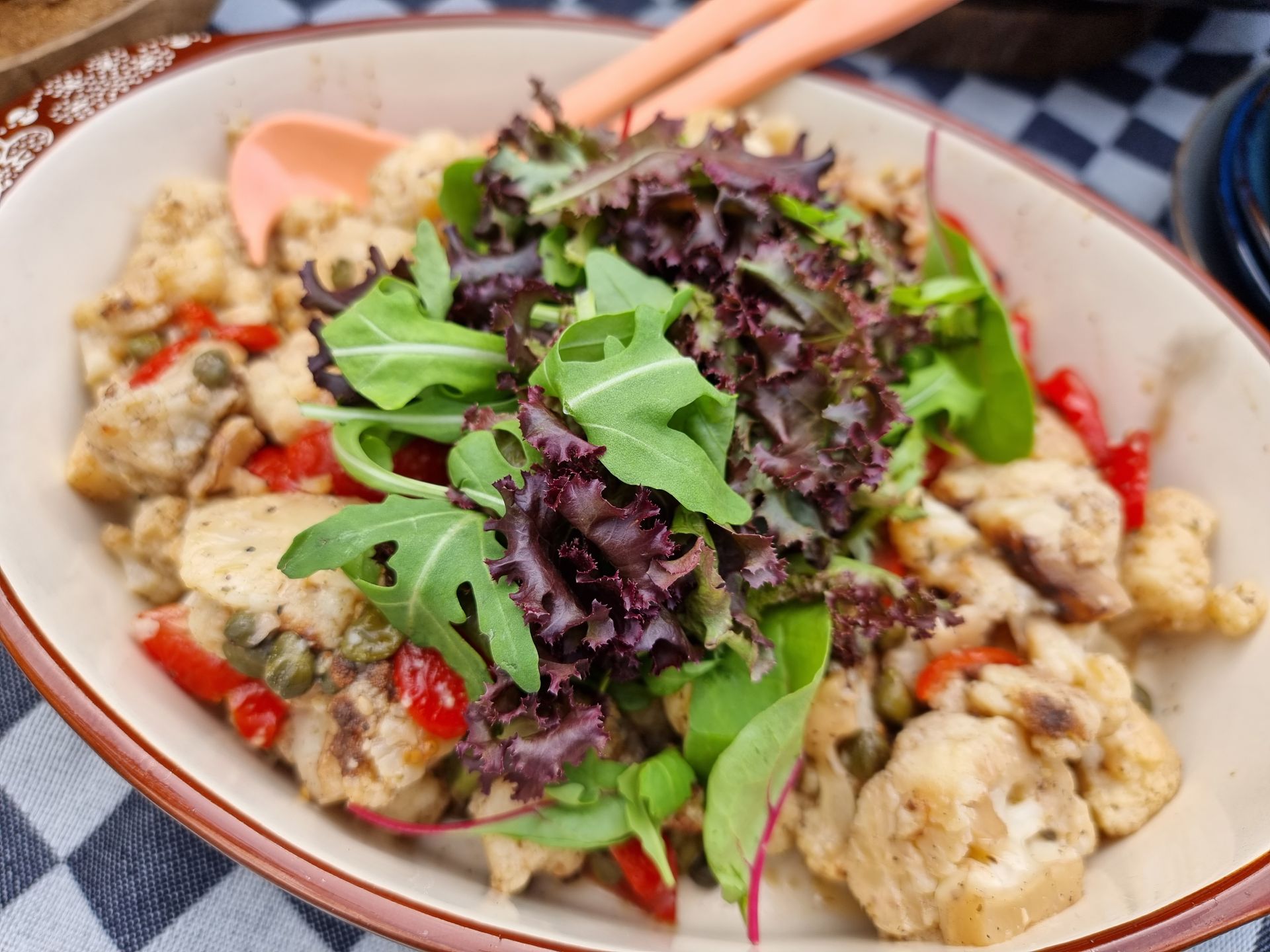 Bloemkool, paprika en kappertjes in een kom, gegarneerd met gemengde sla.
