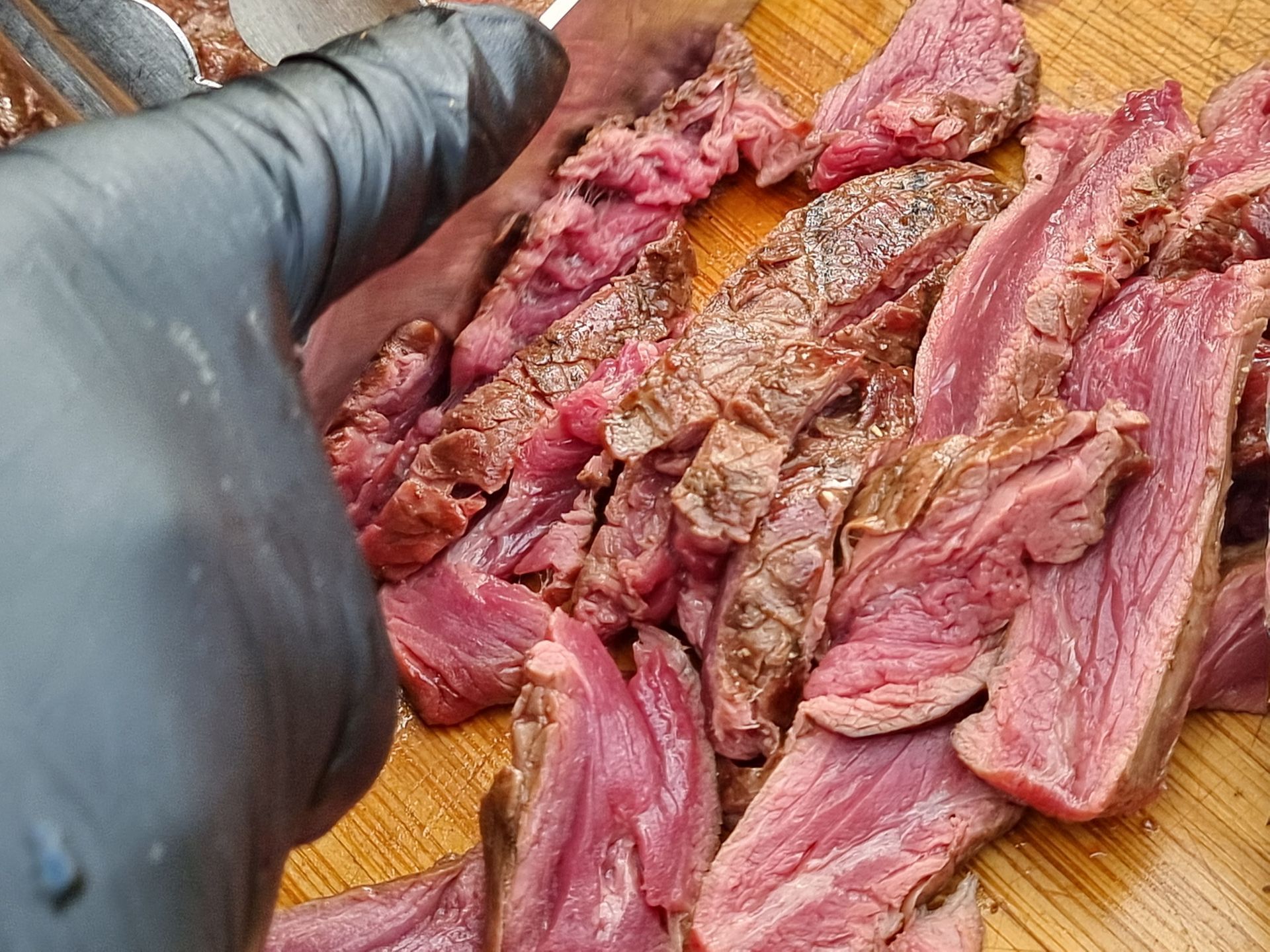 Een in plakjes gesneden bavette op een houten plank. Het vlees is rosé en medium-rare gebakken.