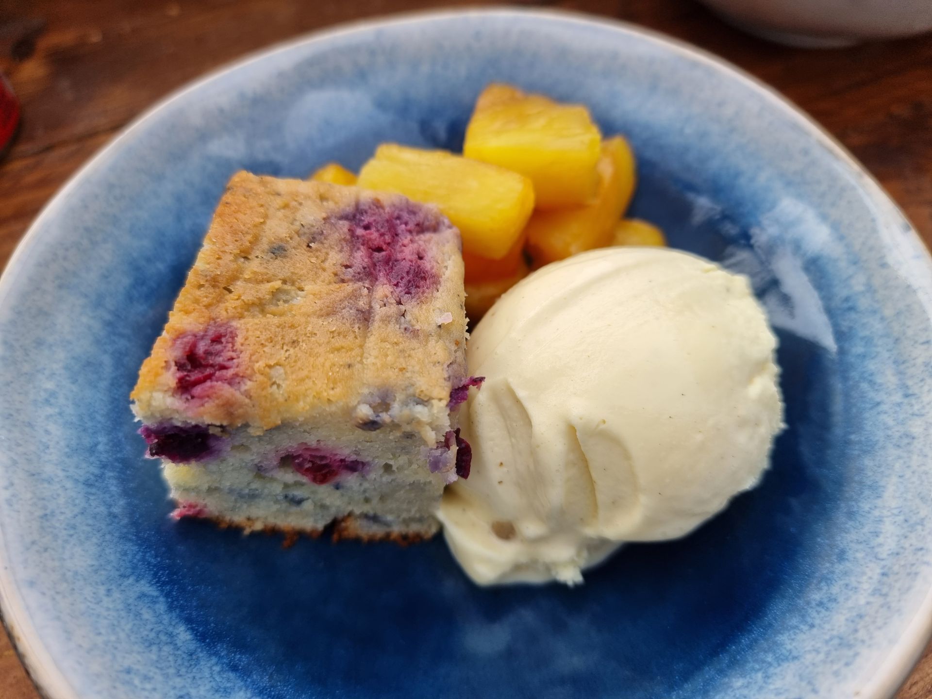 Bosbessentaart, ijs en ananas in een blauw schaaltje.