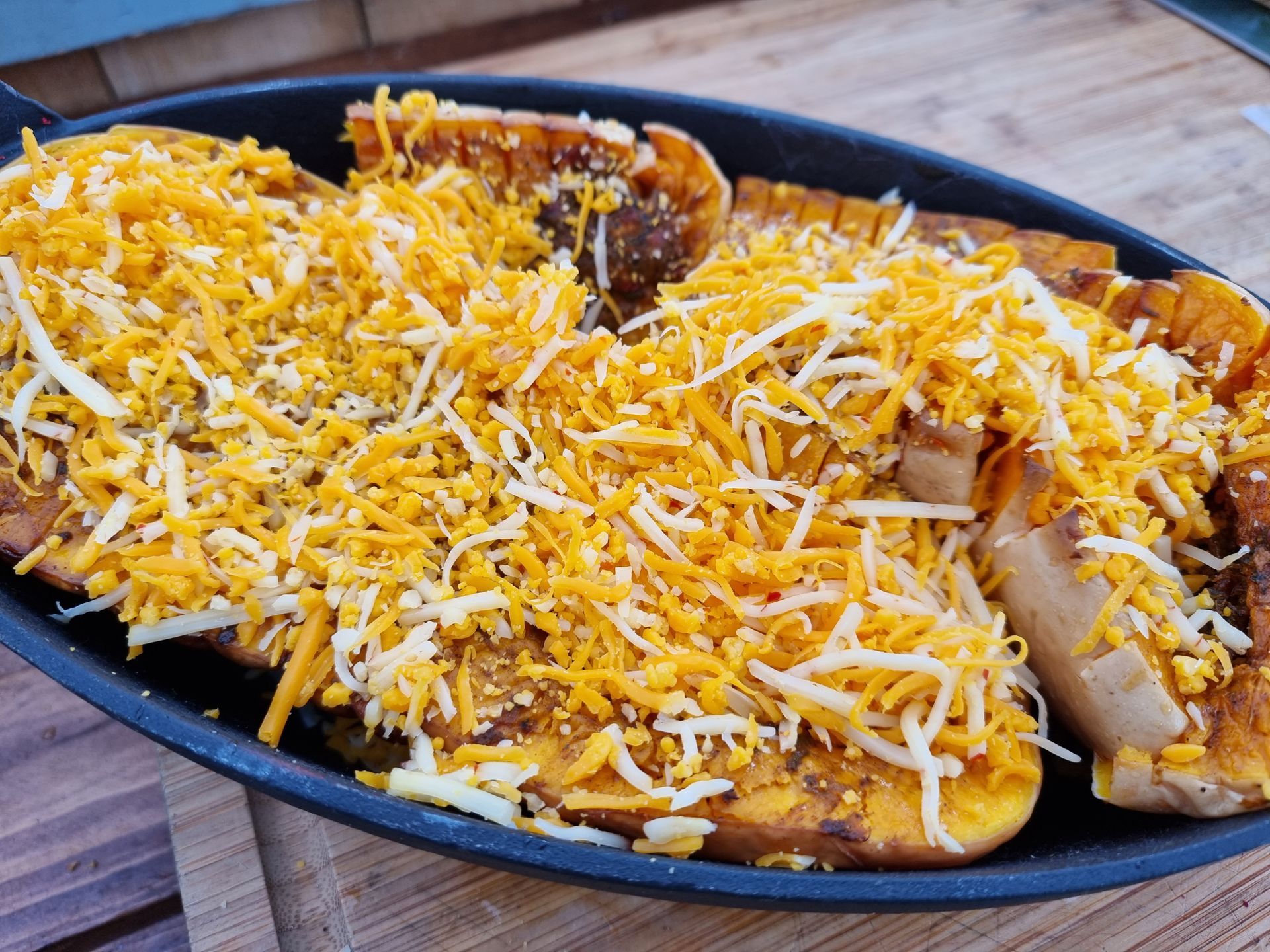Geroosterde flespompoen met geraspte cheddar kaas, geserveerd in een zwarte gietijzeren schaal.