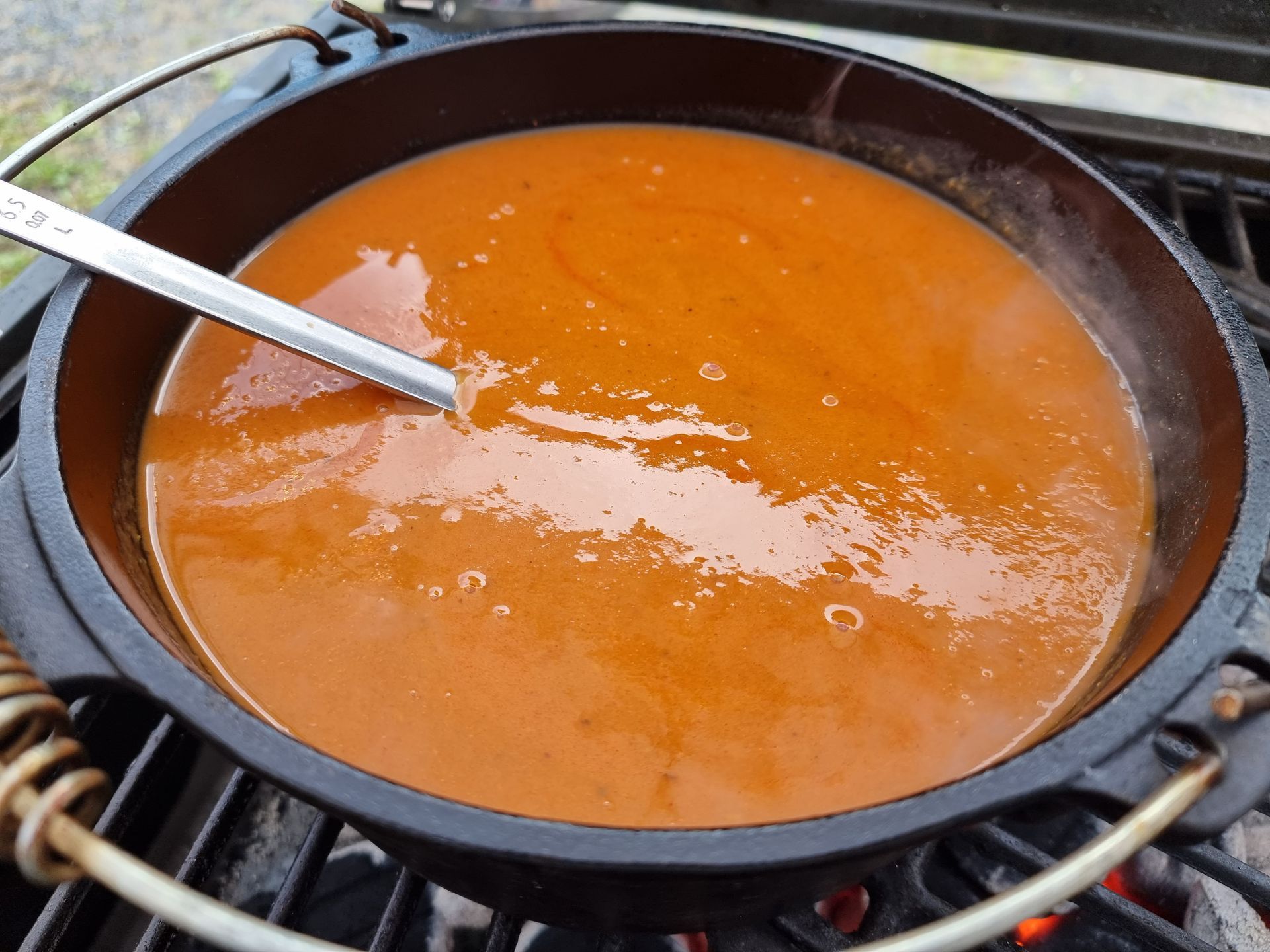 Een braadpan op de grill met tomatensoep, een lepel ligt erin.