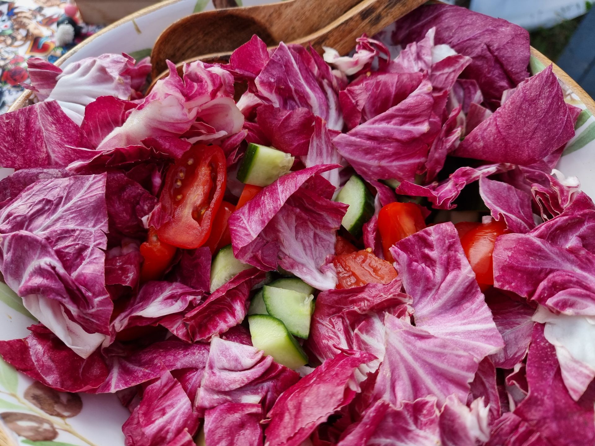 Salade in een kom met rode radicchioblaadjes, plakjes tomaat en stukjes komkommer.