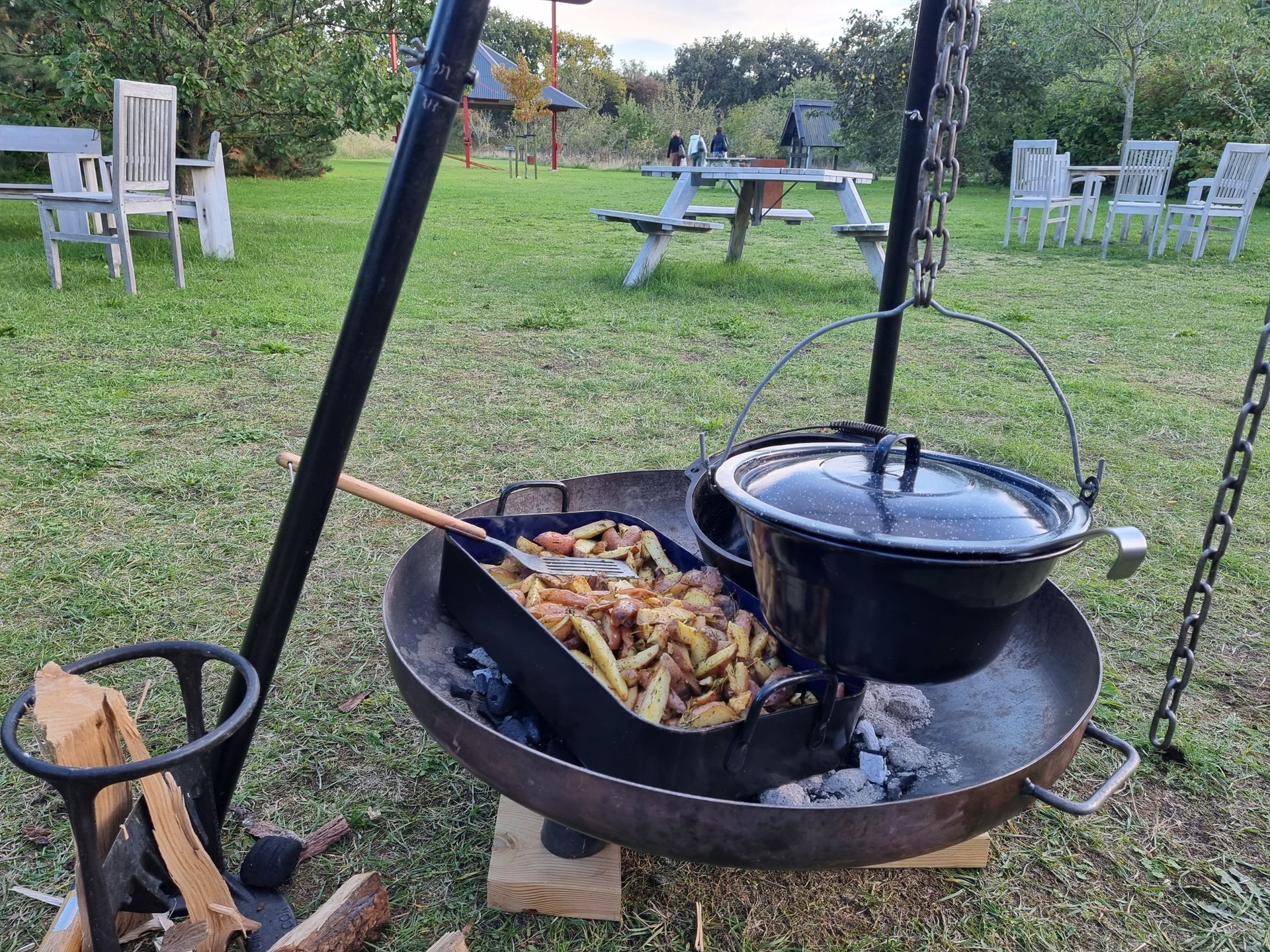 Kookopstelling: aardappelen in een grote pan boven een vuur, een zwarte pot, op een driepoot barbecue.