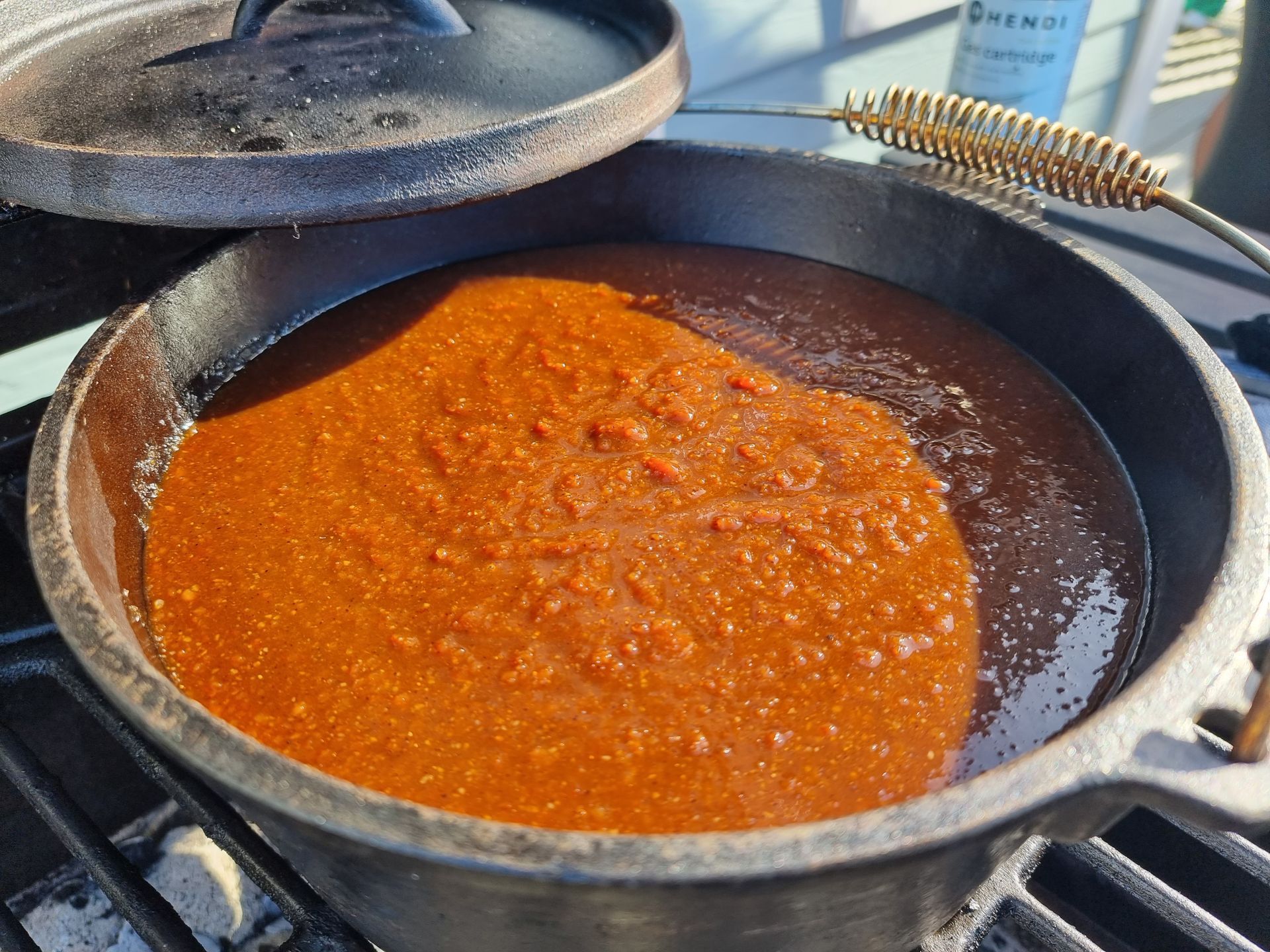 Gietijzeren braadpan met sudderende saus. Het deksel staat er gedeeltelijk open bovenop.
