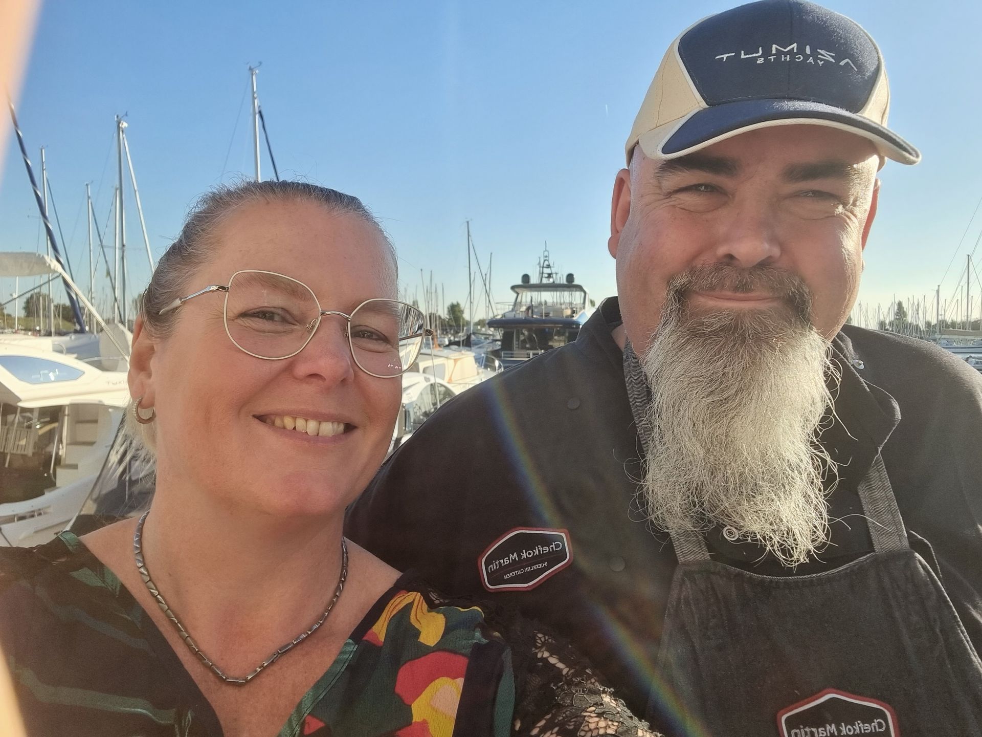 Chefkok MArtin en Mirjam op een zonnige dag in een haven met boten op de achtergrond.