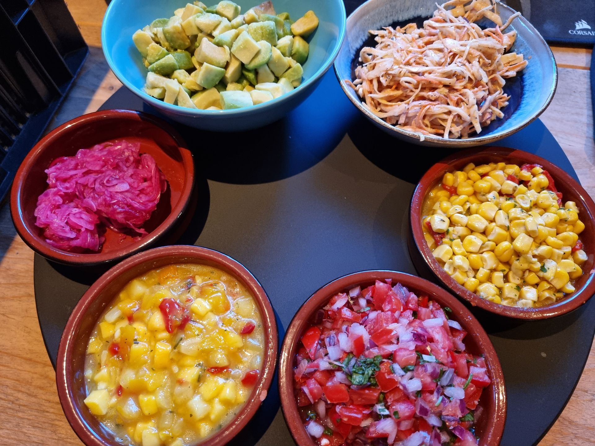 Zeven schalen met kleurrijke toppings, uitgestald op een zwarte ondergrond. 