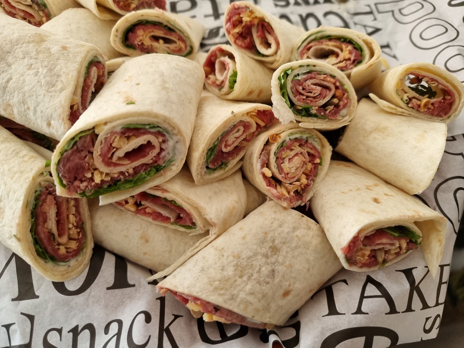 In stukken gesneden tortillawraps gevuld met vlees, kaas en sla, opgestapeld op een met papier bekleed oppervlak.